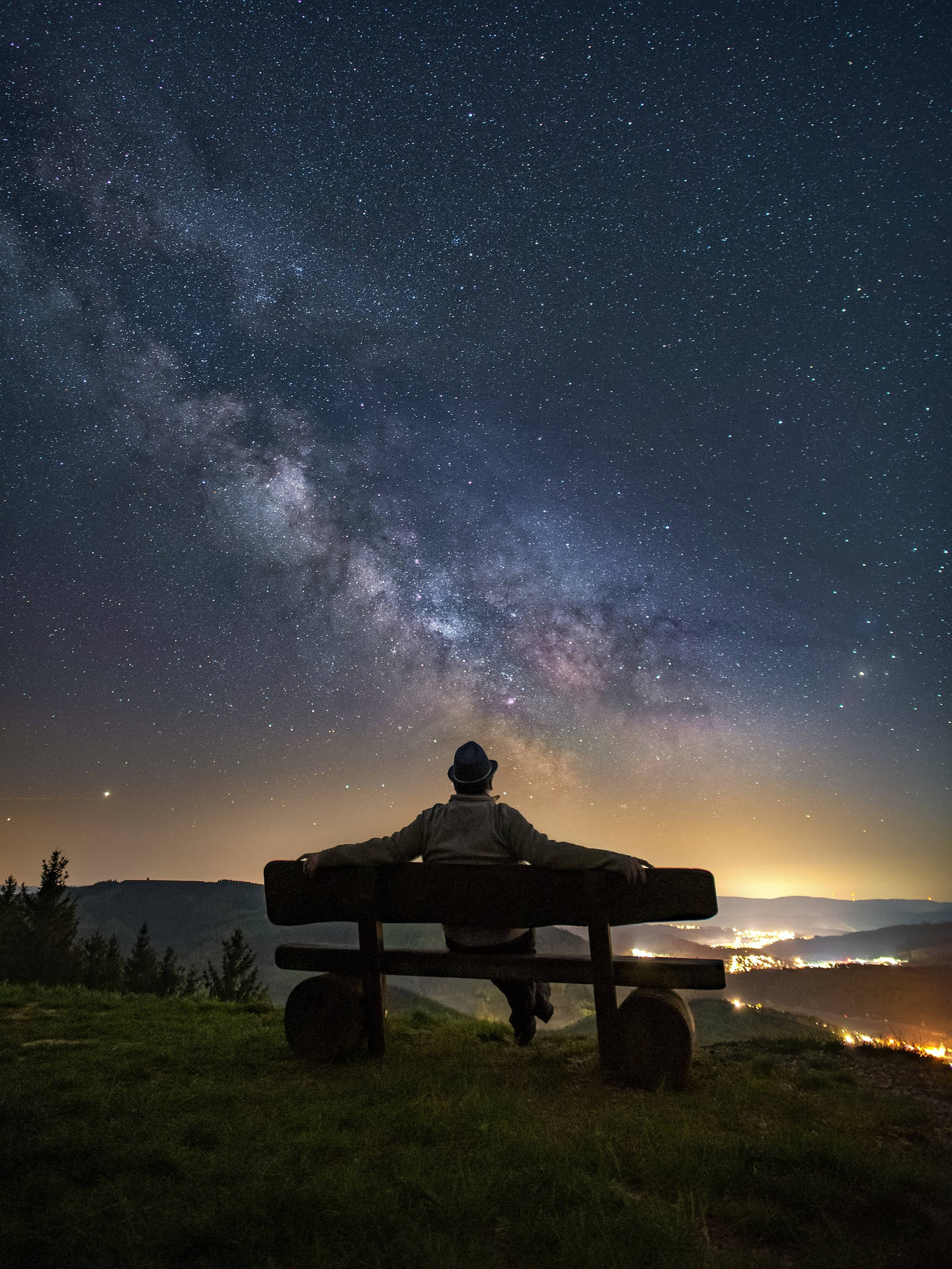 人坐在長椅上，星空下俯瞰山谷燈光