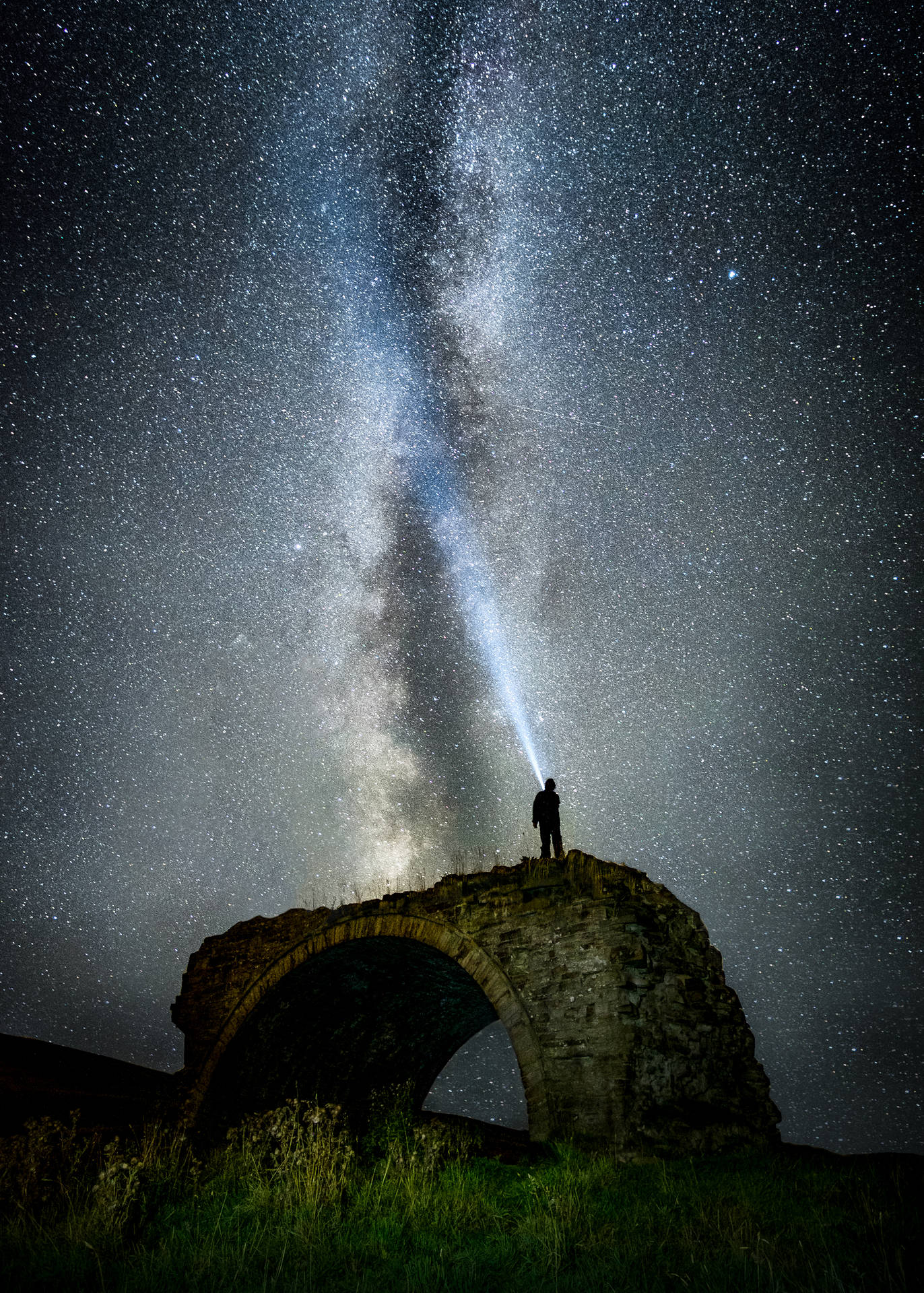 人站在石拱門上用手電筒照向銀河星星