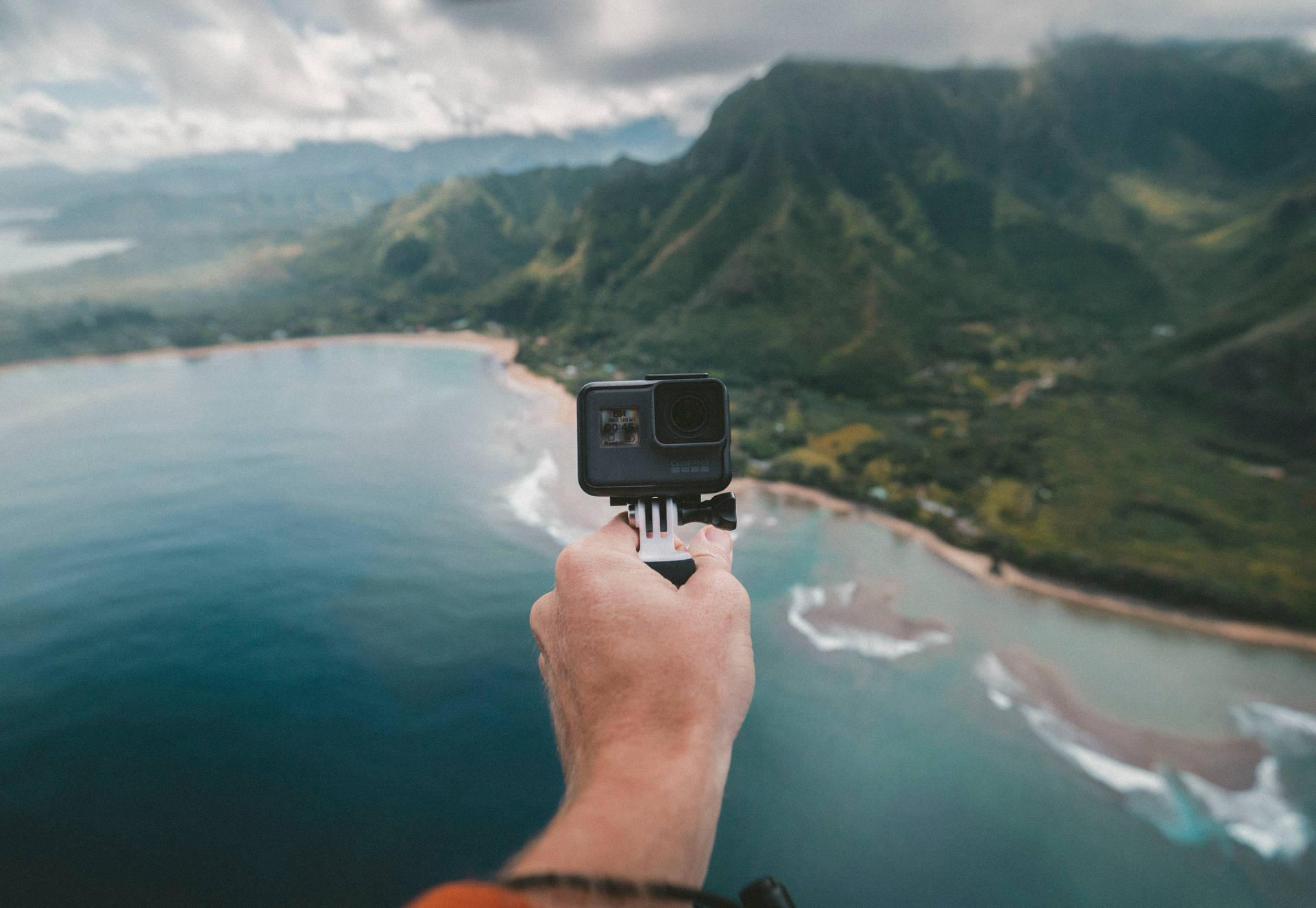 手在海洋和山脈上方拿著GoPro相機