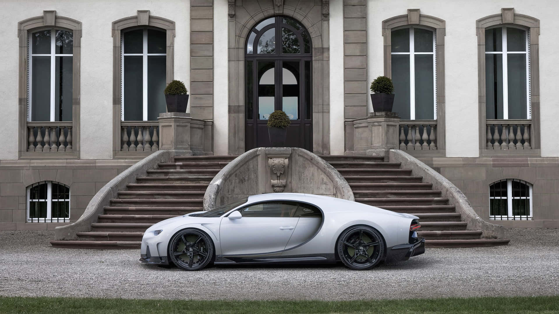 銀色 Bugatti Chiron 停泊在一座宏偉的石砌大宅前，配有拱形窗戶和對稱樓梯。