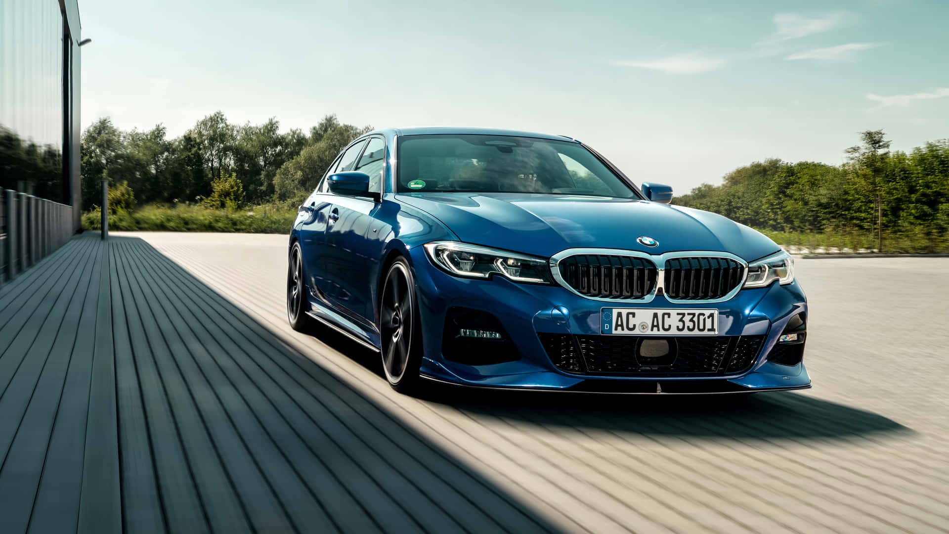 藍色BMW M3轎車停放在木質甲板上，背景有樹木和建築物。