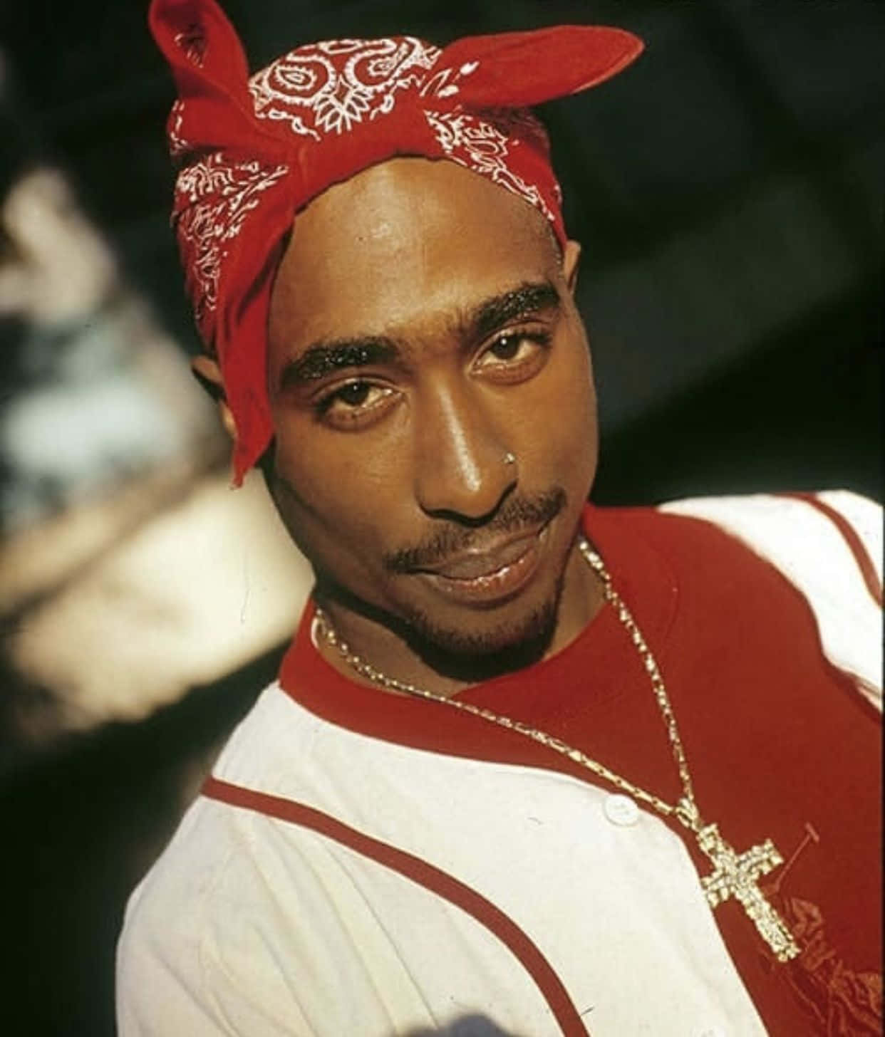 Tupac Shakur 戴著紅色頭巾和金色十字架項鍊的特寫肖像。