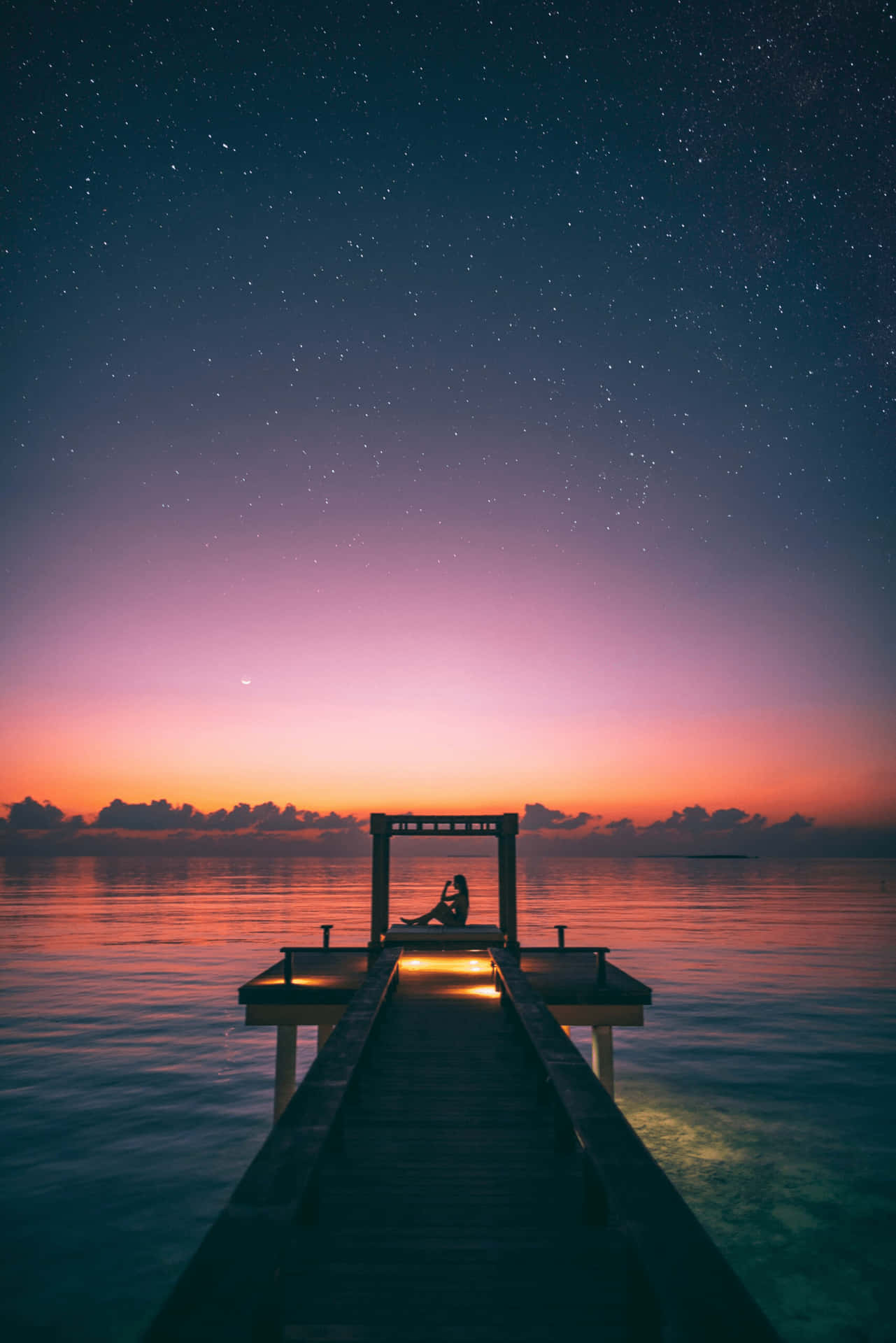 一個人在星空下暮色中坐在燈光碼頭上的剪影。