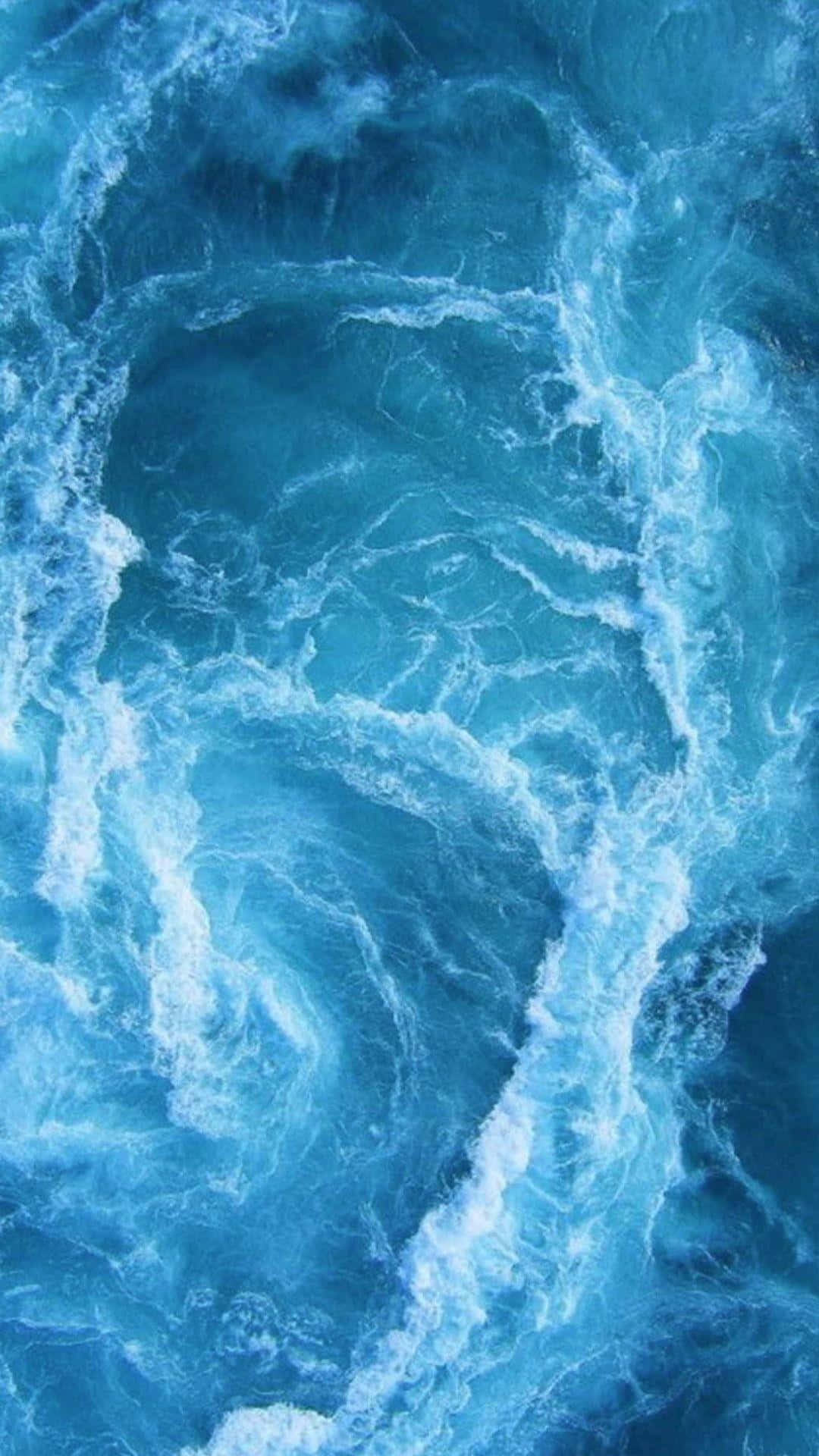 從空中視角看，洶湧的藍色海浪與白色泡沫旋轉。