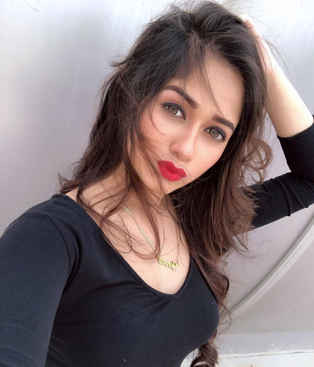 深色頭髮和紅色口紅的女性，身穿黑色上衣，在白色弧形牆前擺姿勢。