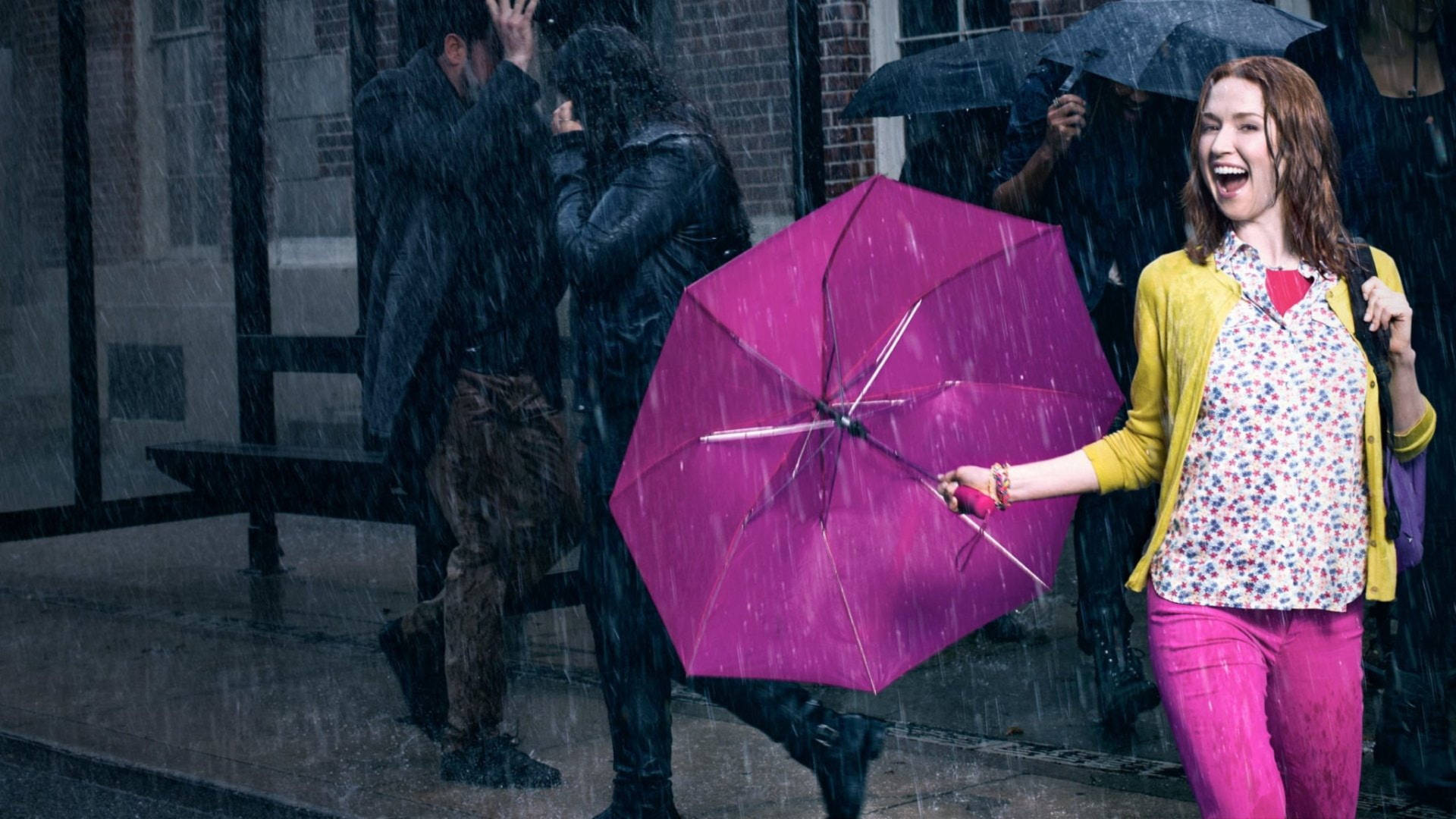 女人在雨中的城市街道上撐著粉紅色雨傘大笑，其他人看起來很惱火。