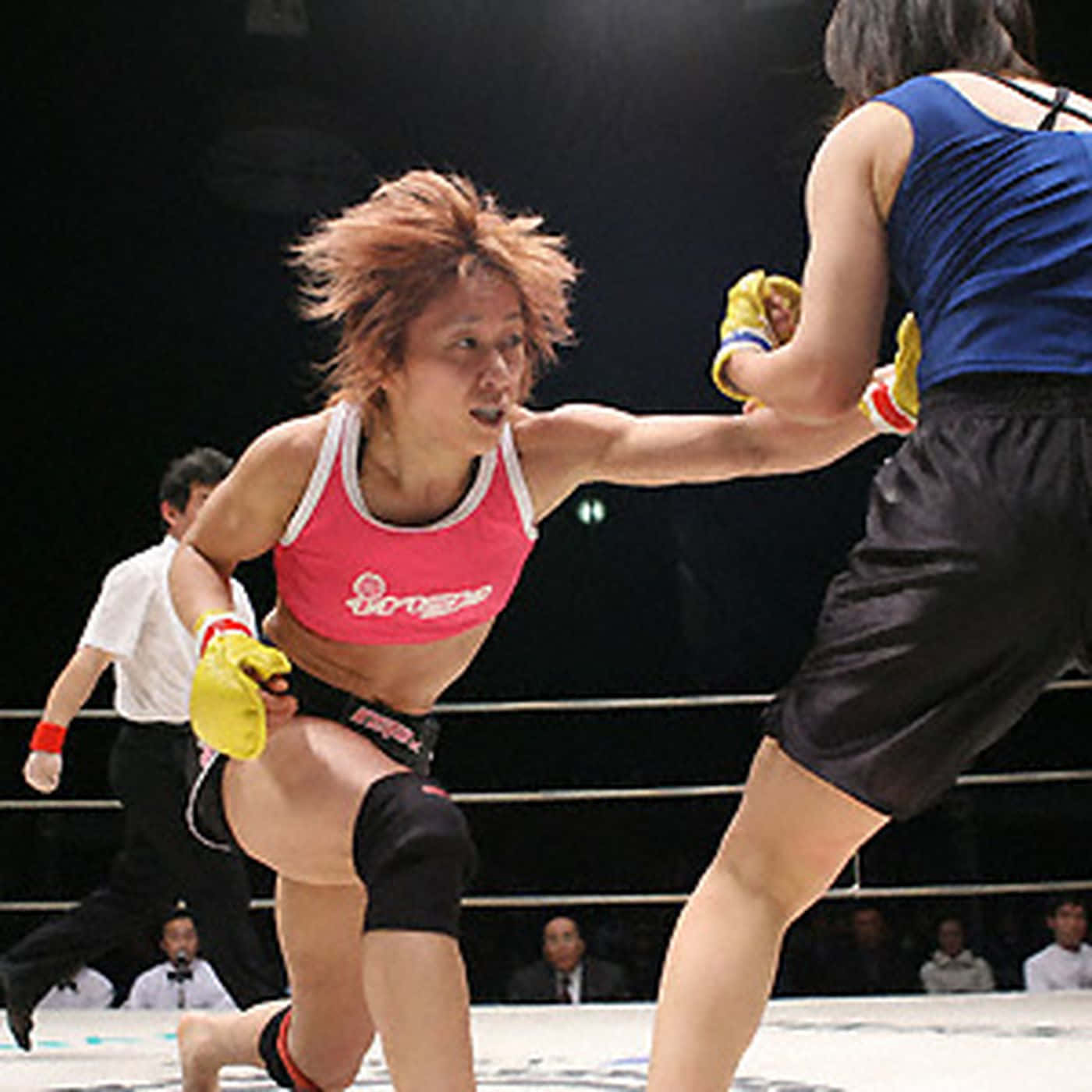 無畏的梅古美·藤井對戰麗莎·沃德 壁紙 — 兩名女拳手在燈光明亮的擂台上交鋒，其中一人身穿粉紅色上衣和黃色手套向前猛衝。