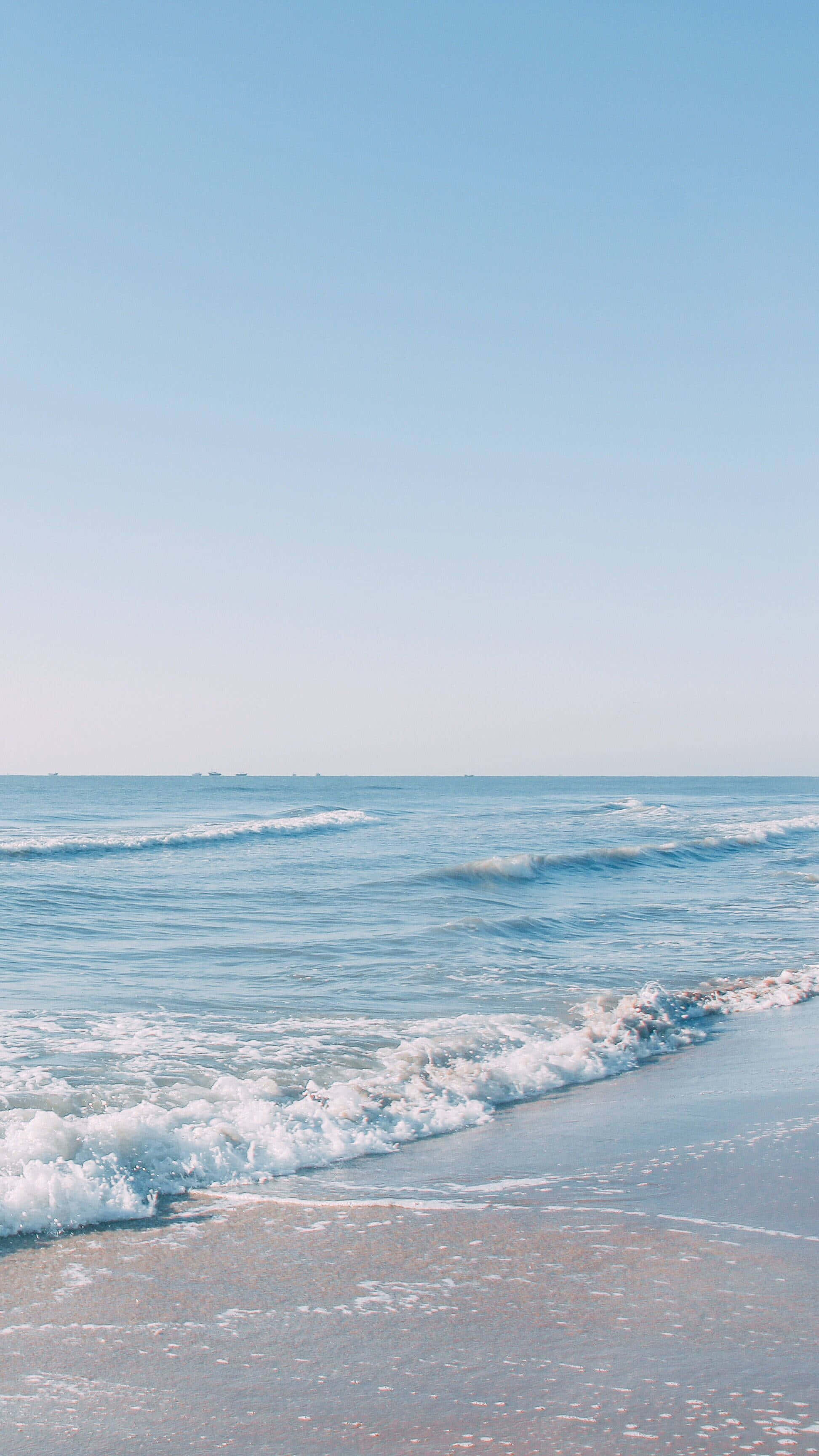 無盡海天交界線 壁紙 — 平靜的海浪在清澈的藍天下輕輕拍打著沙灘。