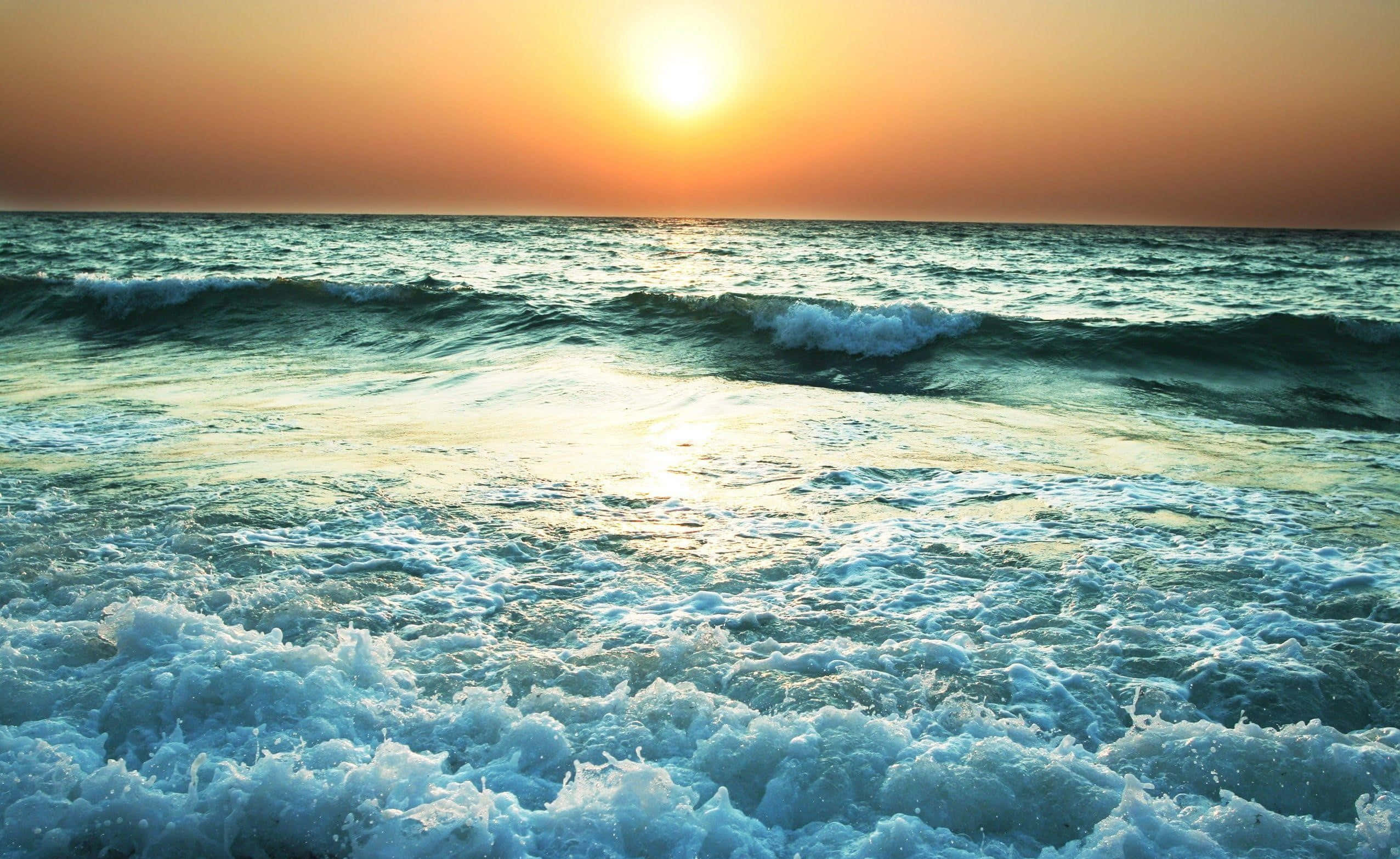 無盡海洋，無限可能 壁紙 — 夕陽在翻滾的海浪上投下金色光芒，伴隨著白色泡沫和碧綠的海水。
