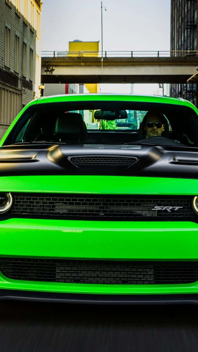 無聊的綠色汽車 壁紙 — 一輛充滿活力的綠色 Dodge Challenger SRT 在混凝土天橋下的城市峽谷中疾馳，司機戴著太陽眼鏡。