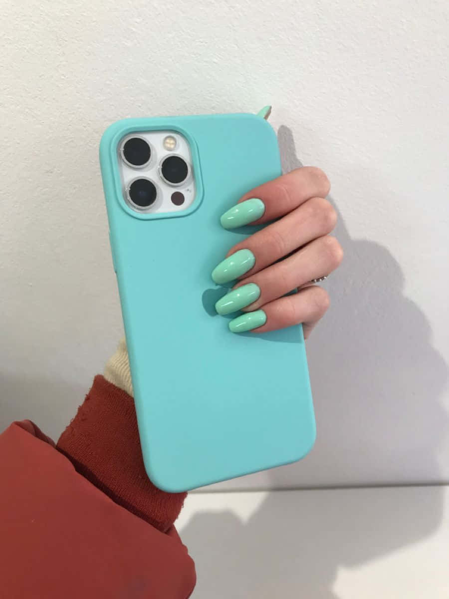 無與倫比的 iPhone 12 壁紙 — 一隻帶有薄荷綠色指甲的手拿著淺藍色手機殼，靠在純白牆上。