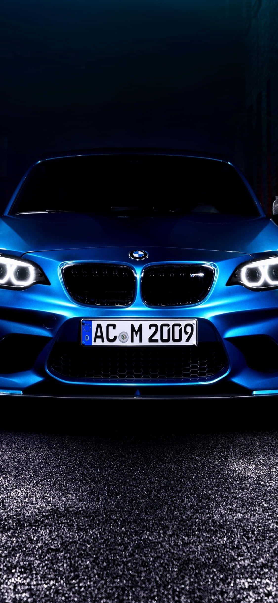 無與倫比的奢華與品質——iPhone X與BMW 壁紙 — 一輛引人注目的藍色BMW M2跑車在戲劇性燈光下，在帶有反射瀝青的黑暗背景中閃耀。