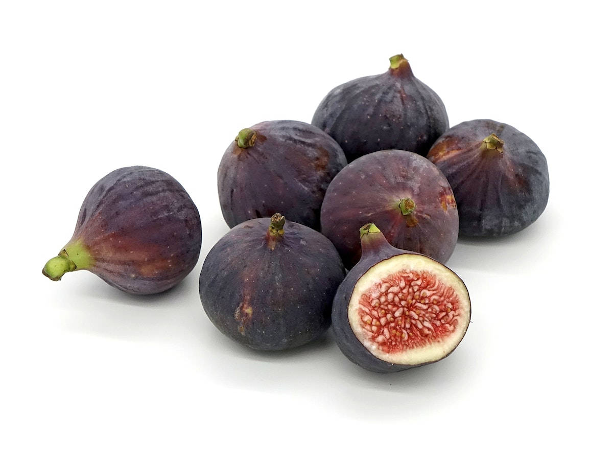 無花果 Ficus Carica 純白背景 壁紙 — 一串成熟的紫色無花果，其中一個切開一半，露出粉紅色果肉和種子，背景為純白色。