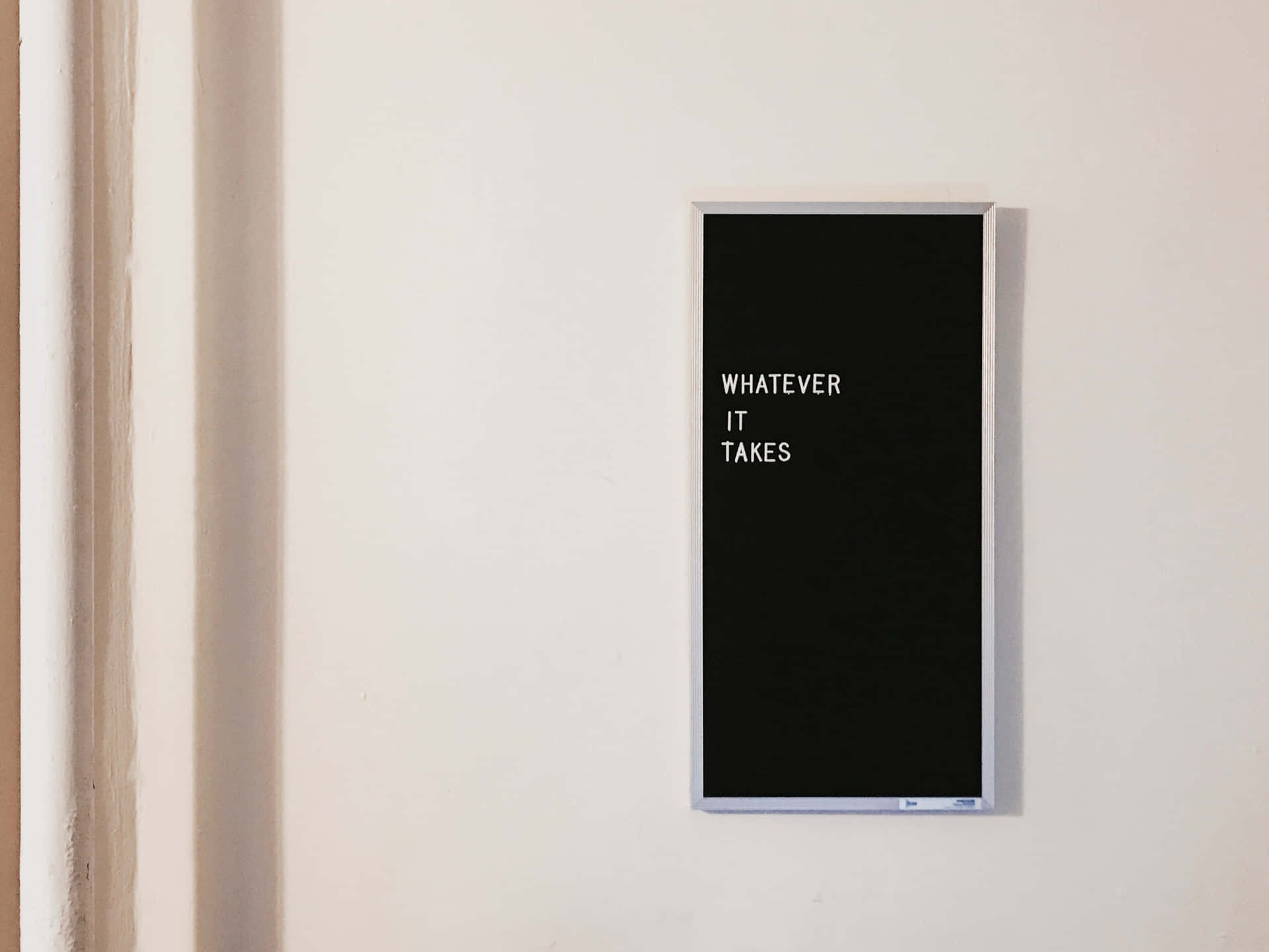 一個黑色邊框的勵志語錄標牌，上面寫著「WHATEVER IT TAKES」，位於白色牆上。
