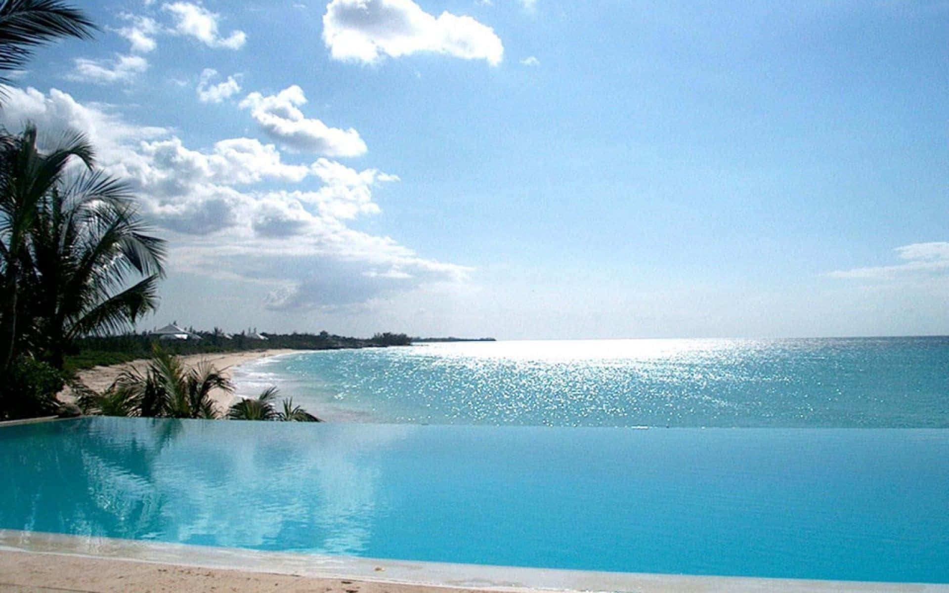 Bahamas Beach 桌布 壁紙 — 無邊際泳池與碧藍海洋無縫融合，上方是點綴著蓬鬆白雲的明亮藍天。