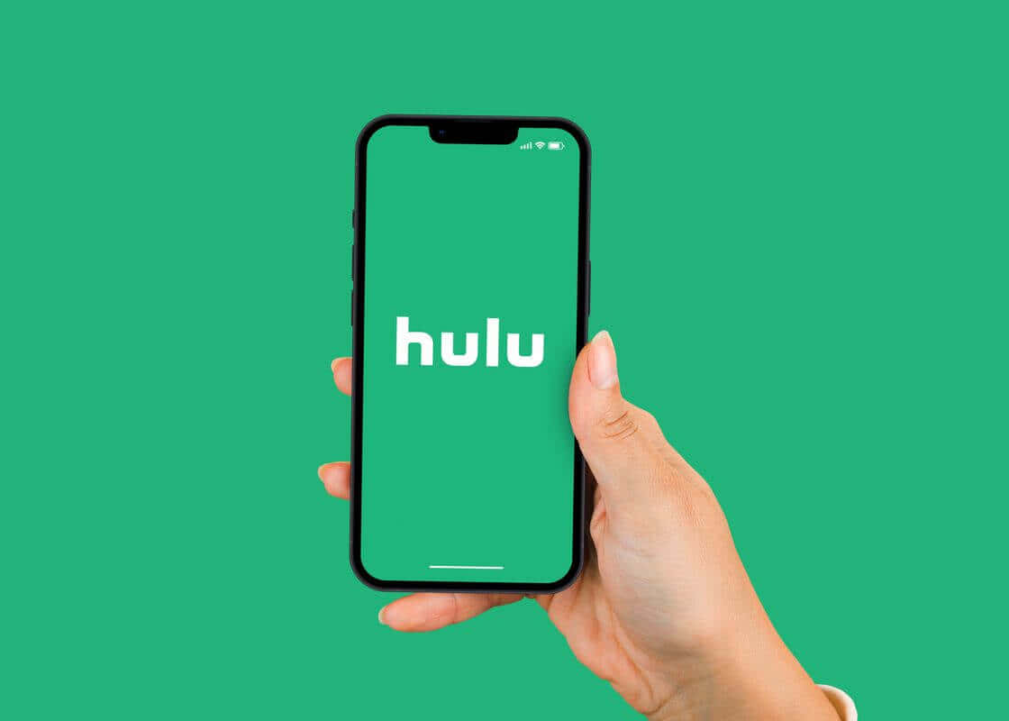 無限串流可能，盡在 Hulu 壁紙 — 一隻手拿著智能手機，在純綠色背景上顯示Hulu標誌。