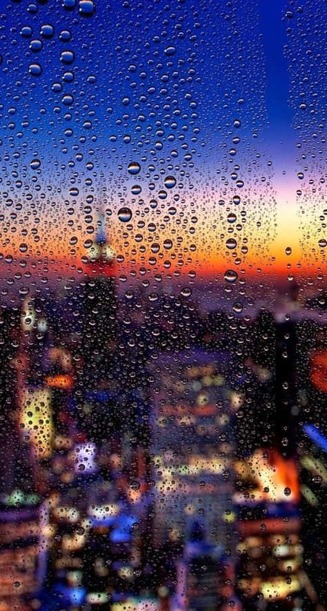 日落時分，橙色和藍色天空下，俯瞰城市的窗戶上的雨滴。