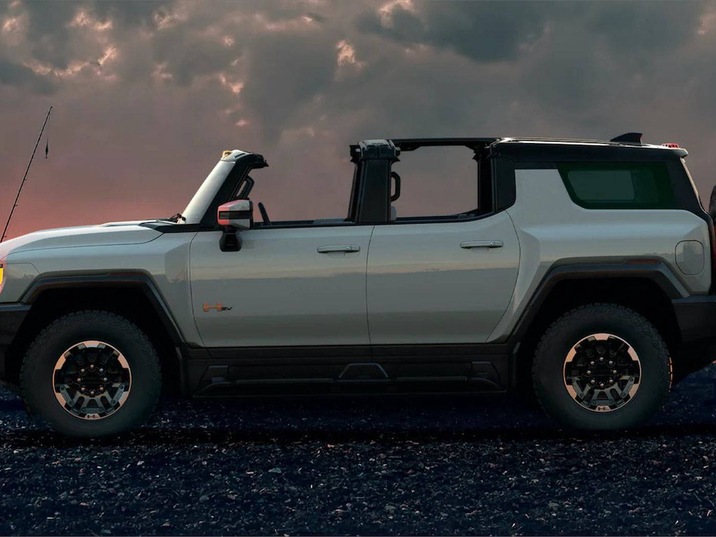 暮色中碎石上的銀色電動Hummer EV，伴隨著色彩繽紛的雲彩。
