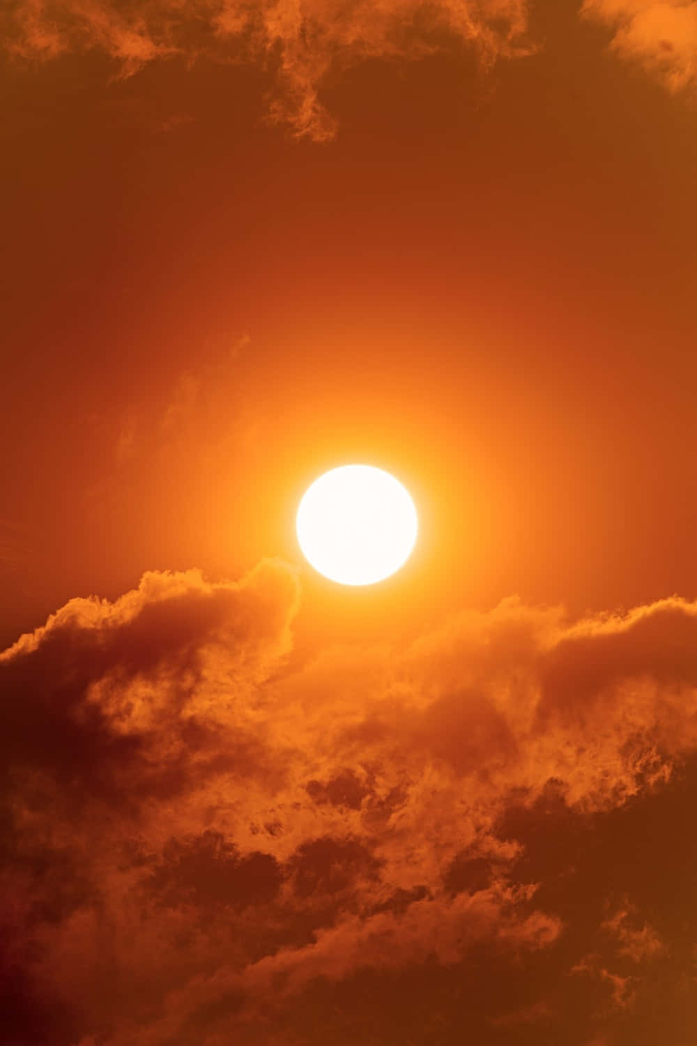 焦糖橙色背景，雲層與太陽 壁紙 — 一顆燦爛的太陽在熾熱的橙色雲層中強烈發光，構成戲劇性的日落天空。