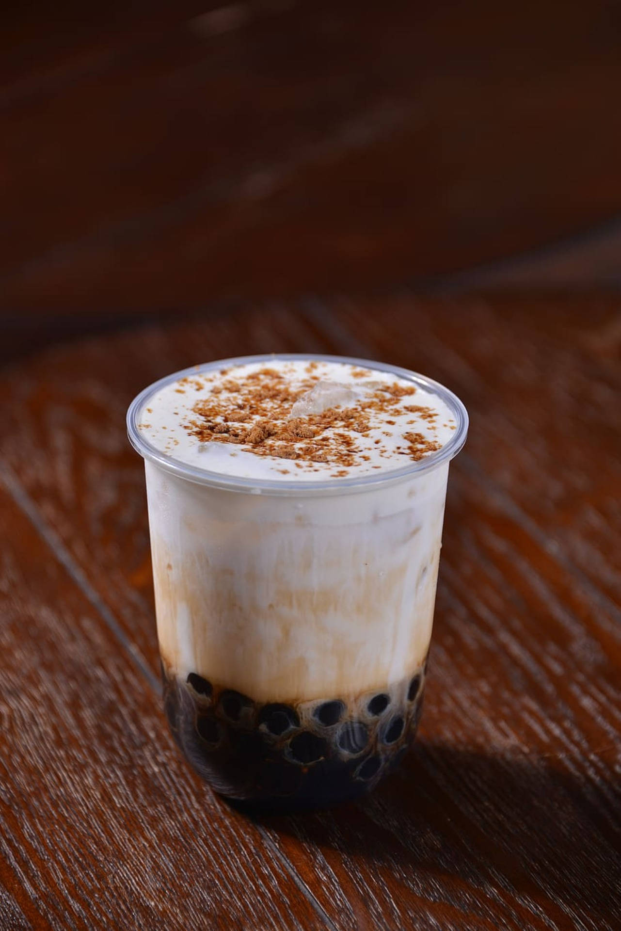 焦糖珍珠奶茶 壁紙 — 一杯奶油冰珍珠奶茶，上面有朱古力碎，放在透明杯裡，置於深棕色木桌上。