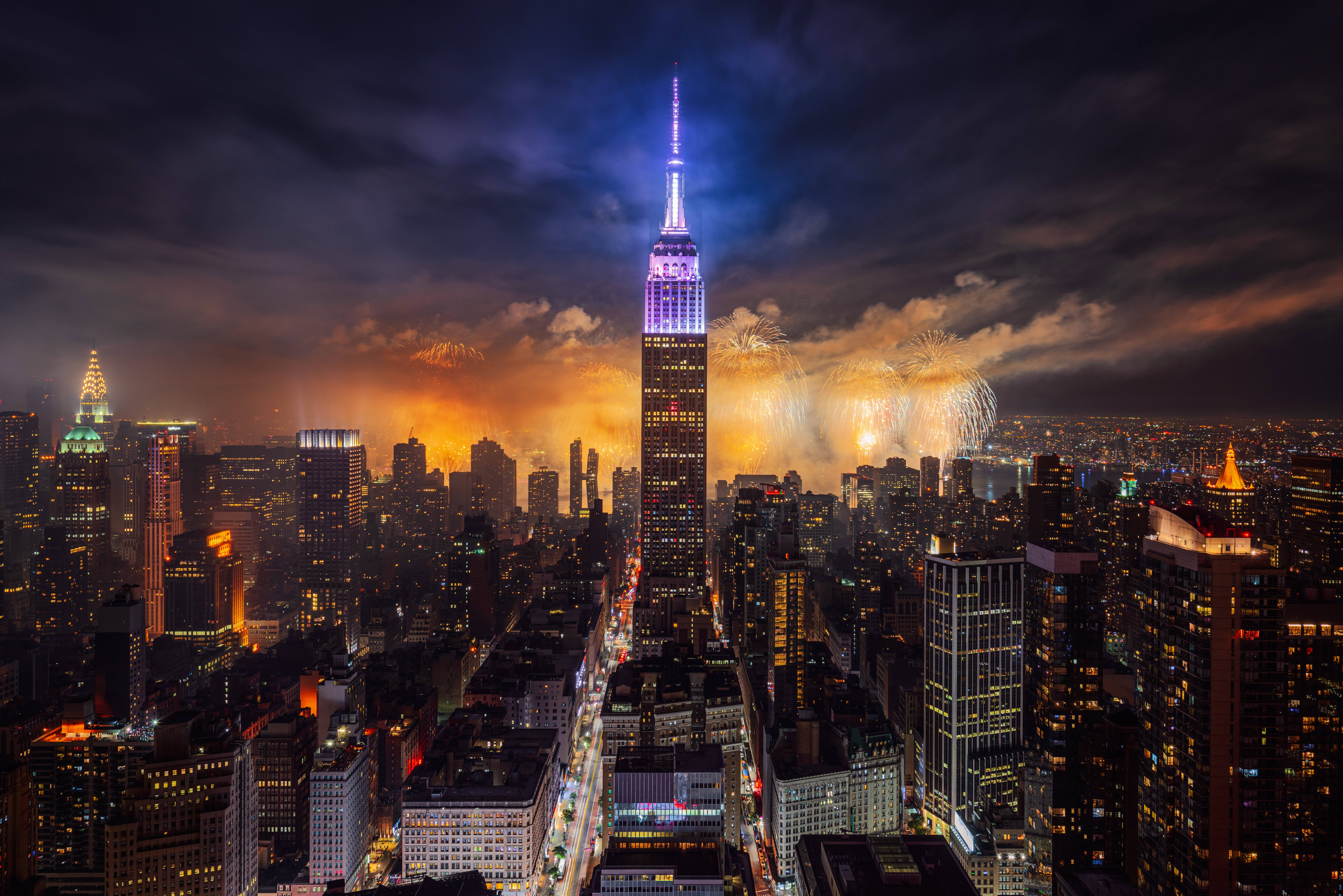 煙火灑落帝國大廈 壁紙 — 紐約令人目眩的夜景，帝國大廈燈火通明，煙火在天空中綻放。