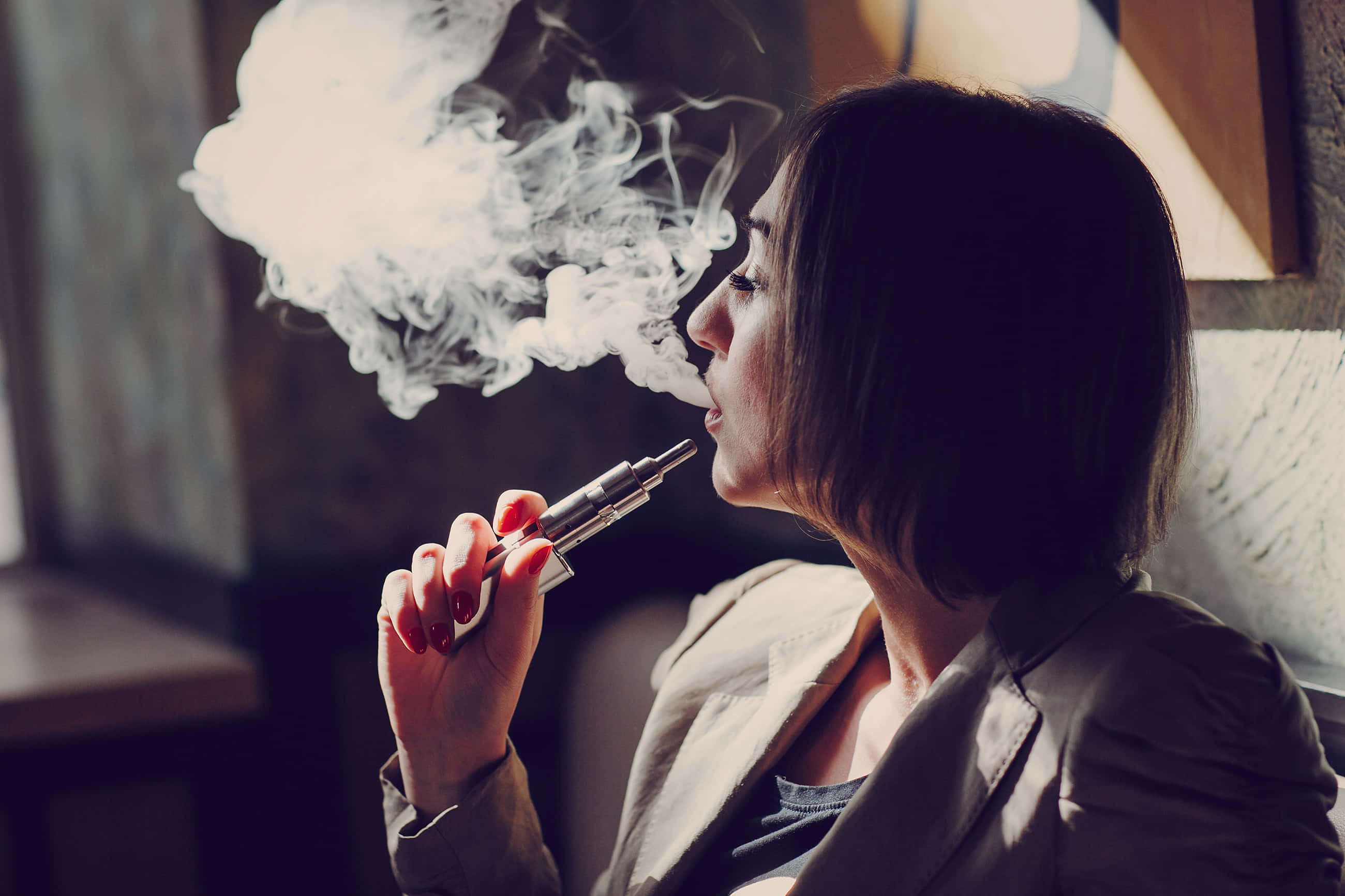 煙草圖片 壁紙 — 一位女性在光線昏暗的室內環境中手持電子煙，呼出一團濃厚的蒸氣。