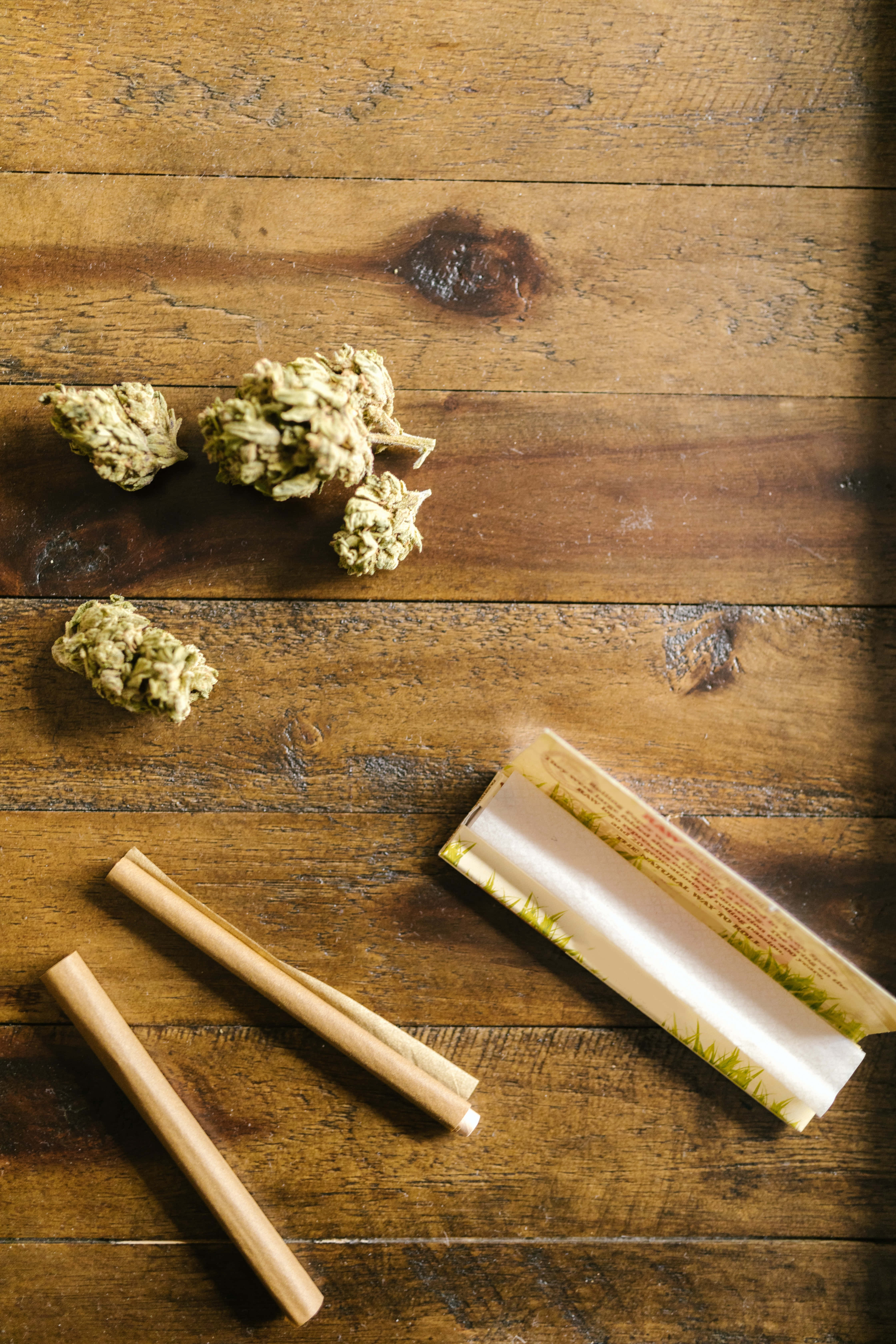煙草的製作材料 壁紙 — 乾燥大麻花蕾和捲煙紙放在經風化的木質表面上，伴隨溫暖的自然光線。