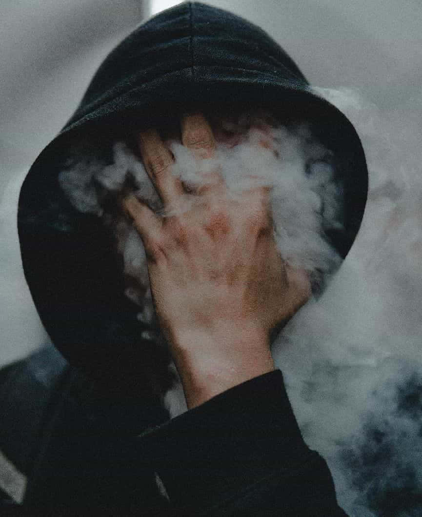 穿著深色連帽衫的人用手遮住臉，白色蒸氣在周圍旋轉。