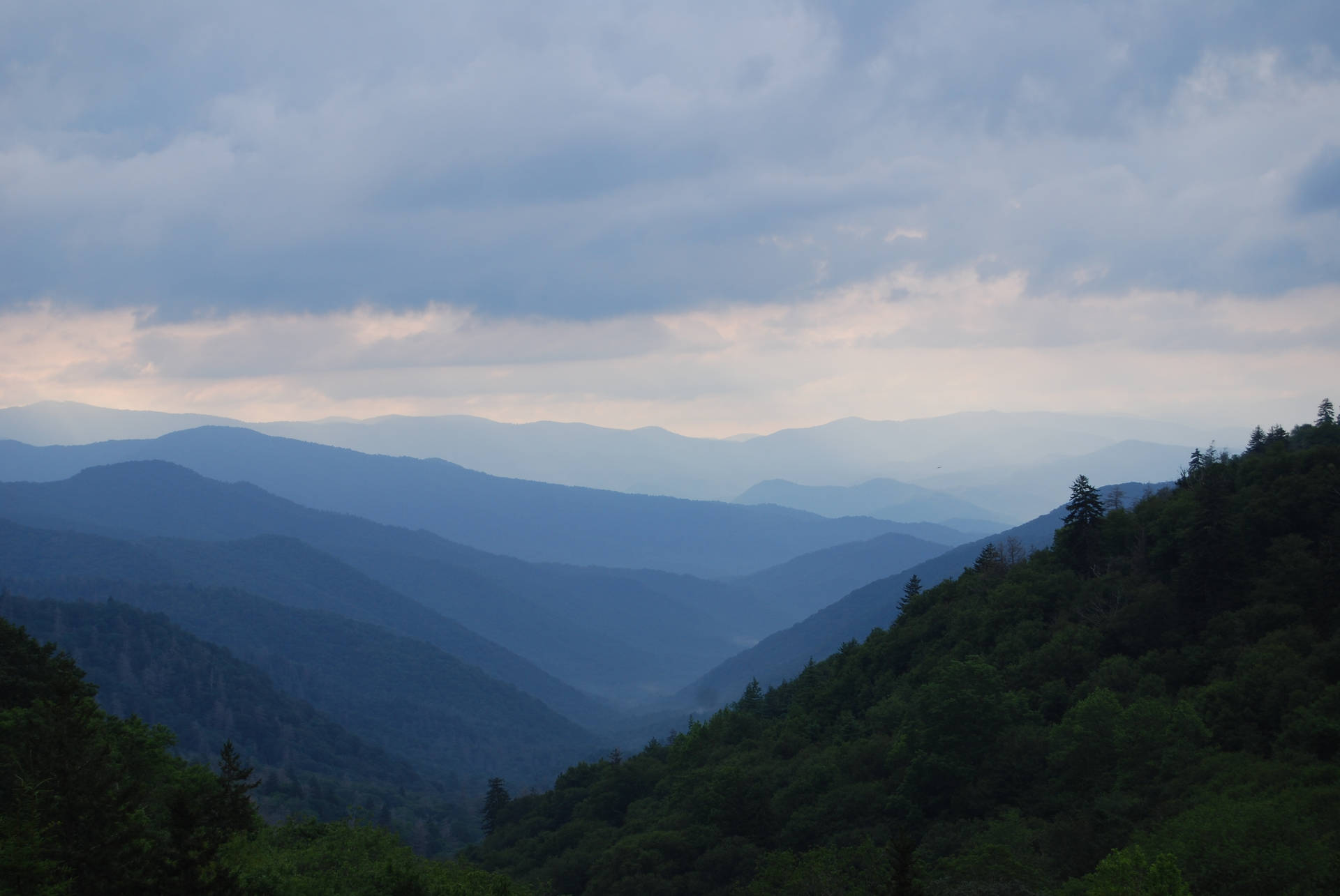 陰雲密布的暮色天空下，層層疊疊的山峰和森林構成的寧靜山景。