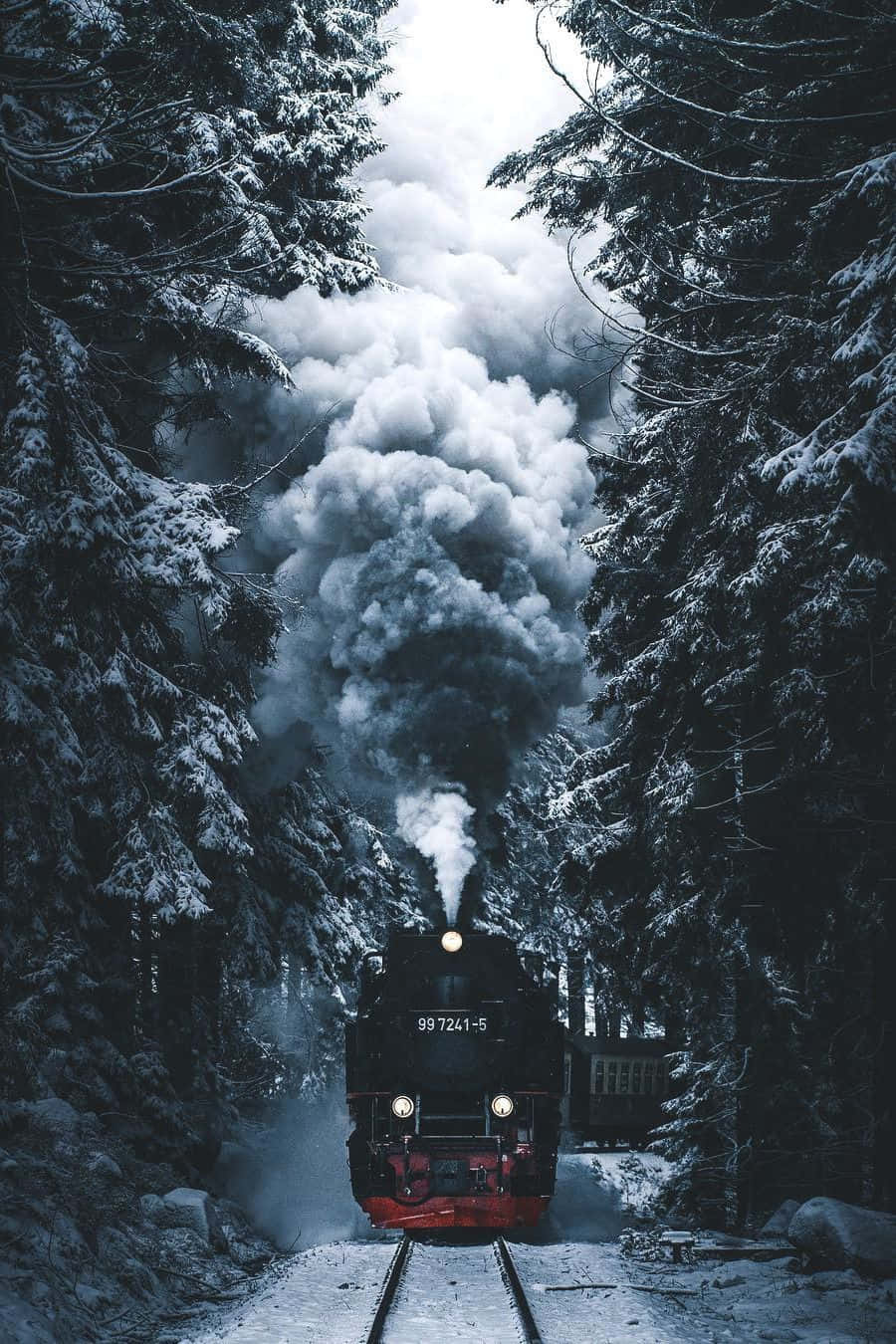 一列蒸汽火車穿過白雪覆蓋的森林，煙霧向上翻騰。