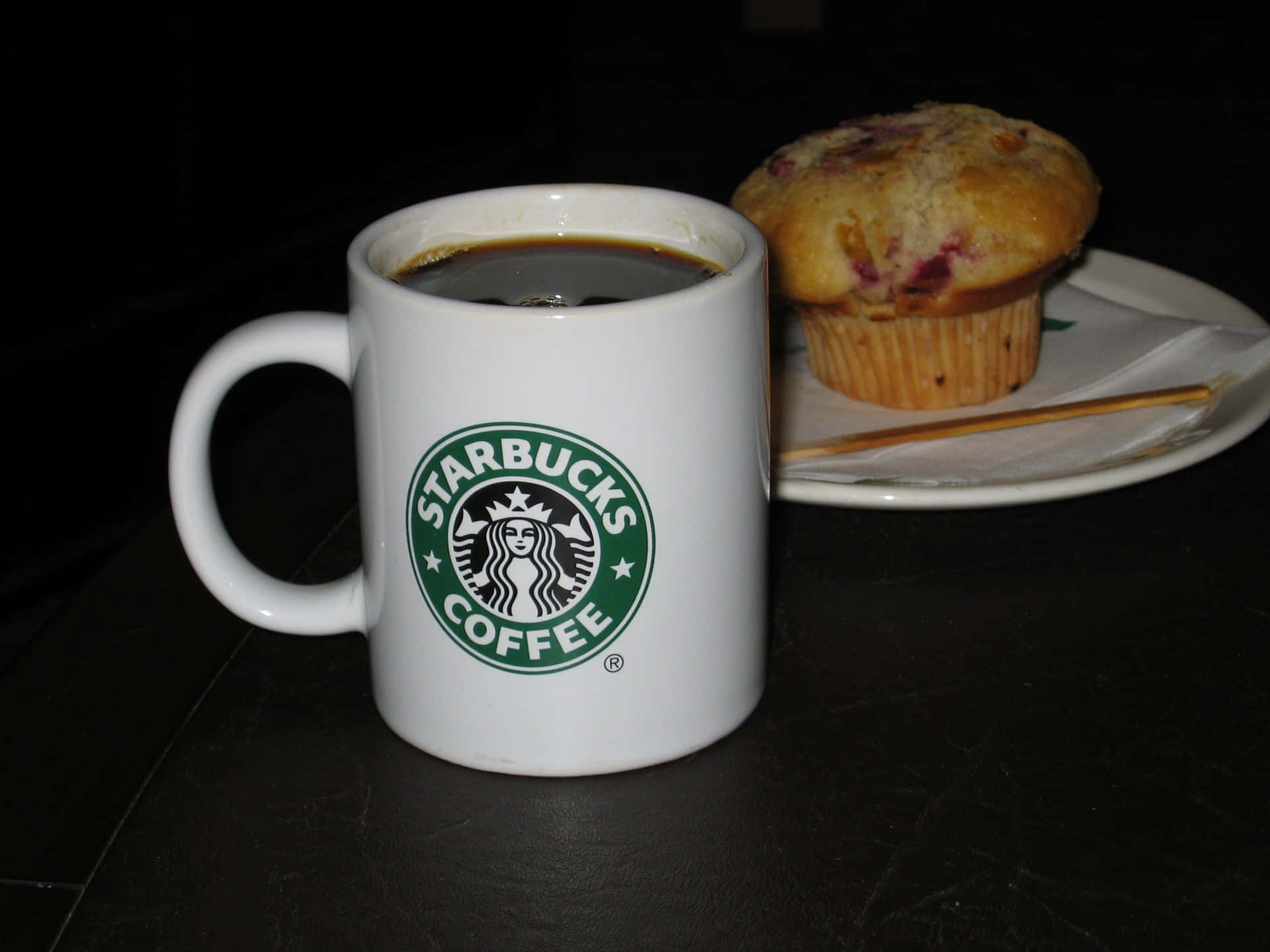 白色Starbucks咖啡杯和莓果鬆餅在深色桌子上。