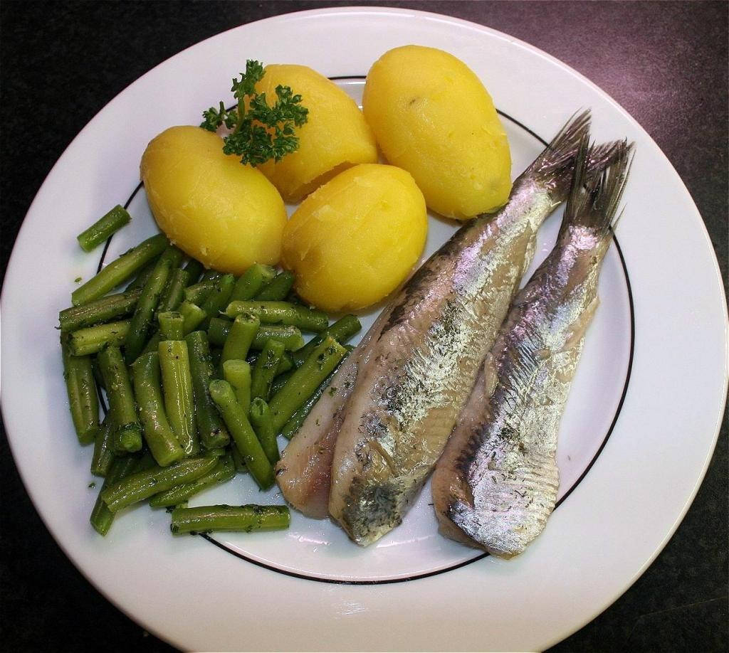 煮熟鯡魚與馬鈴薯 壁紙 — 一個白色碟子盛載兩塊煙燻魚柳，旁邊有烚薯仔和青豆，並以番茜裝飾。