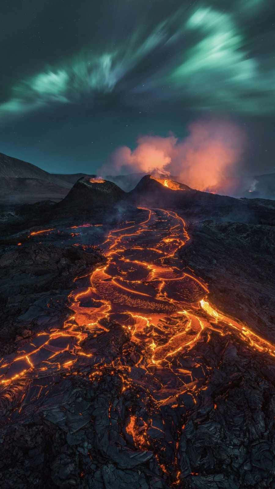 lava 桌布 壁紙 — 熔岩河流發出火熱的橙色光芒，在星空和綠色極光下沿著火山山脈流下。