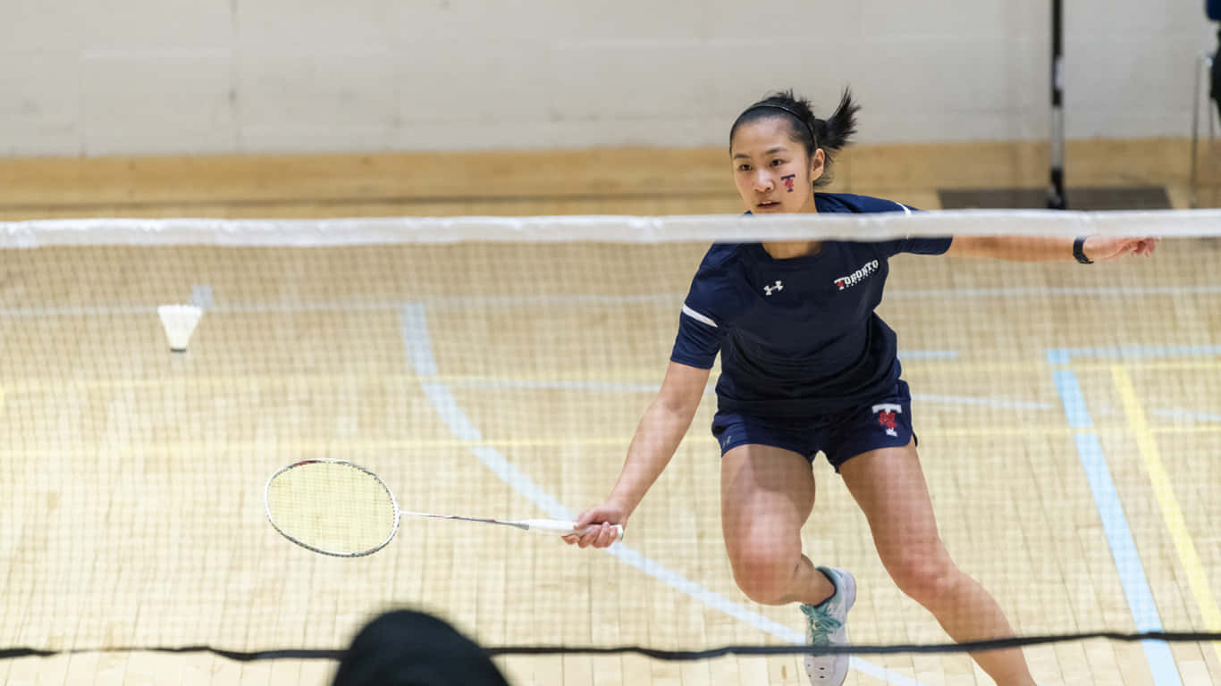 熟能生巧：羽球選手在球場上 壁紙 — 一位專注的女羽毛球手在室內場地揮拍時向前猛衝，羽毛球在空中飛翔。