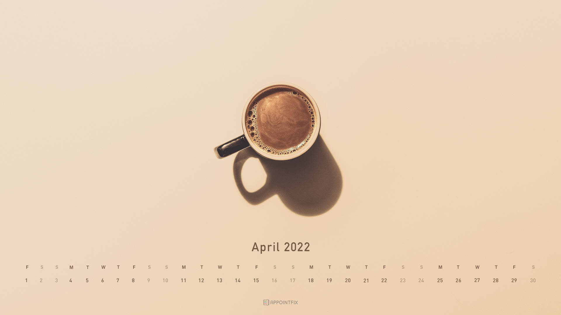 米色背景上，2022年4月日曆上方帶有陰影的咖啡杯。