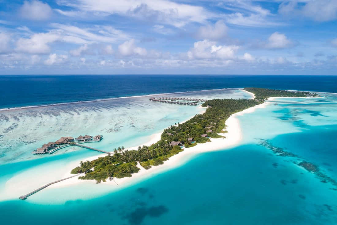 Maldives Island 桌布 壁紙 — 熱帶島嶼度假村的鳥瞰圖，水上小屋和碧綠潟湖在明亮的藍天下。