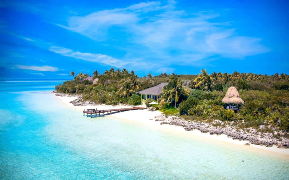 Bahamas Island 桌布 壁紙 — 熱帶島嶼的鳥瞰圖，有碧綠海水、白色沙灘、棕櫚樹和茅草屋頂小屋，在明亮的藍天下。