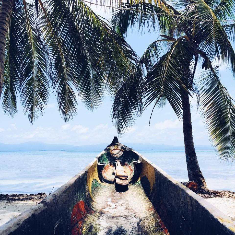 熱帶海灘上棕櫚樹下的彩色獨木舟，背景有海洋和山脈。