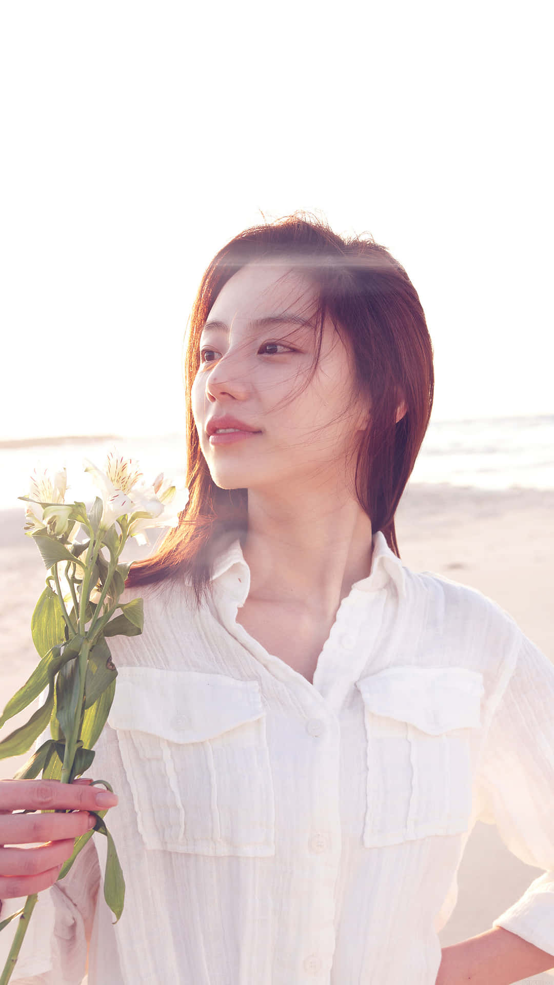 女性在陽光海灘上手持白色花朵