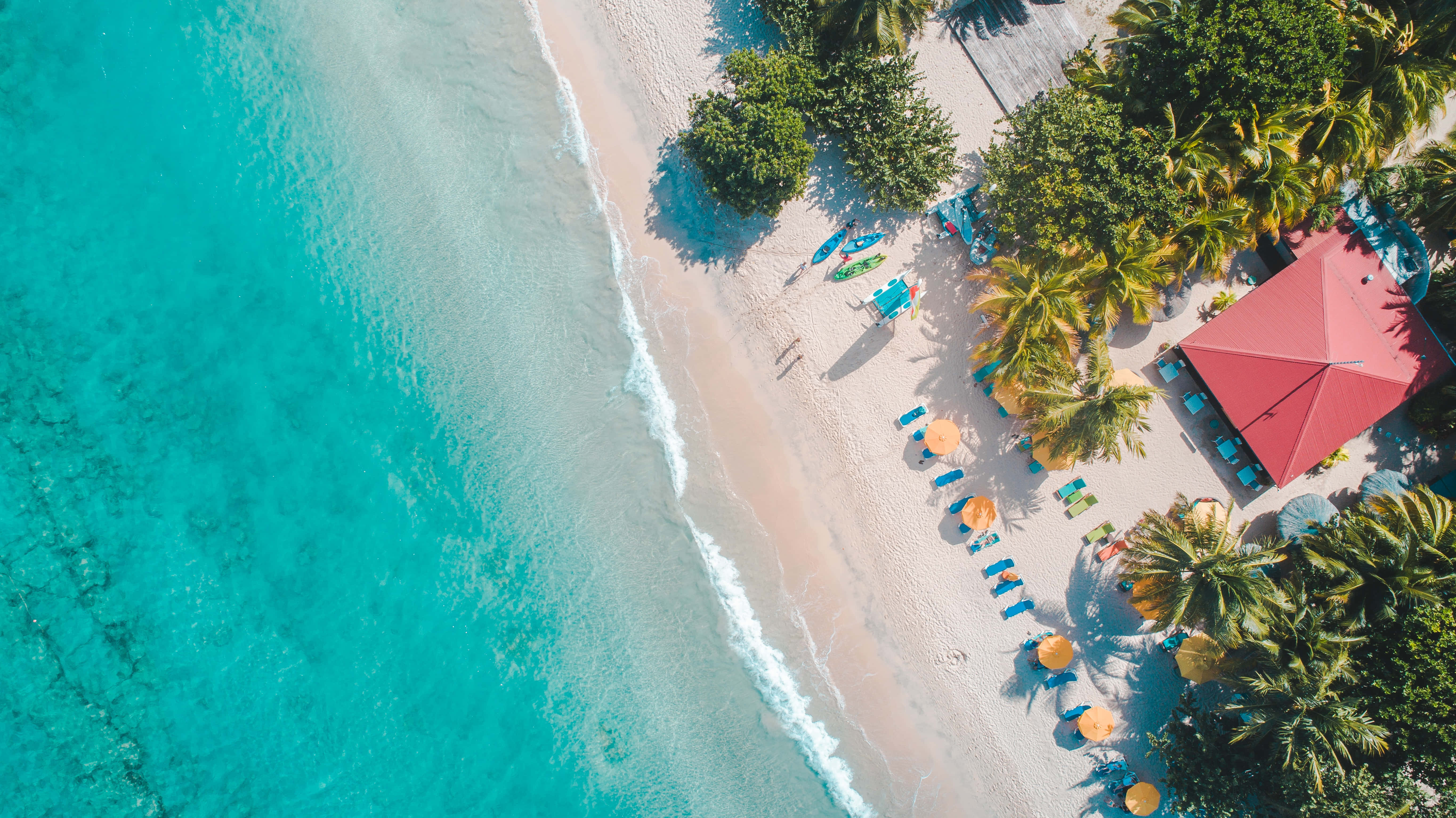 Caribbean 桌布 壁紙 — 熱帶海灘的鳥瞰圖，有碧綠海水、白色沙灘、棕櫚樹和紅頂度假村。