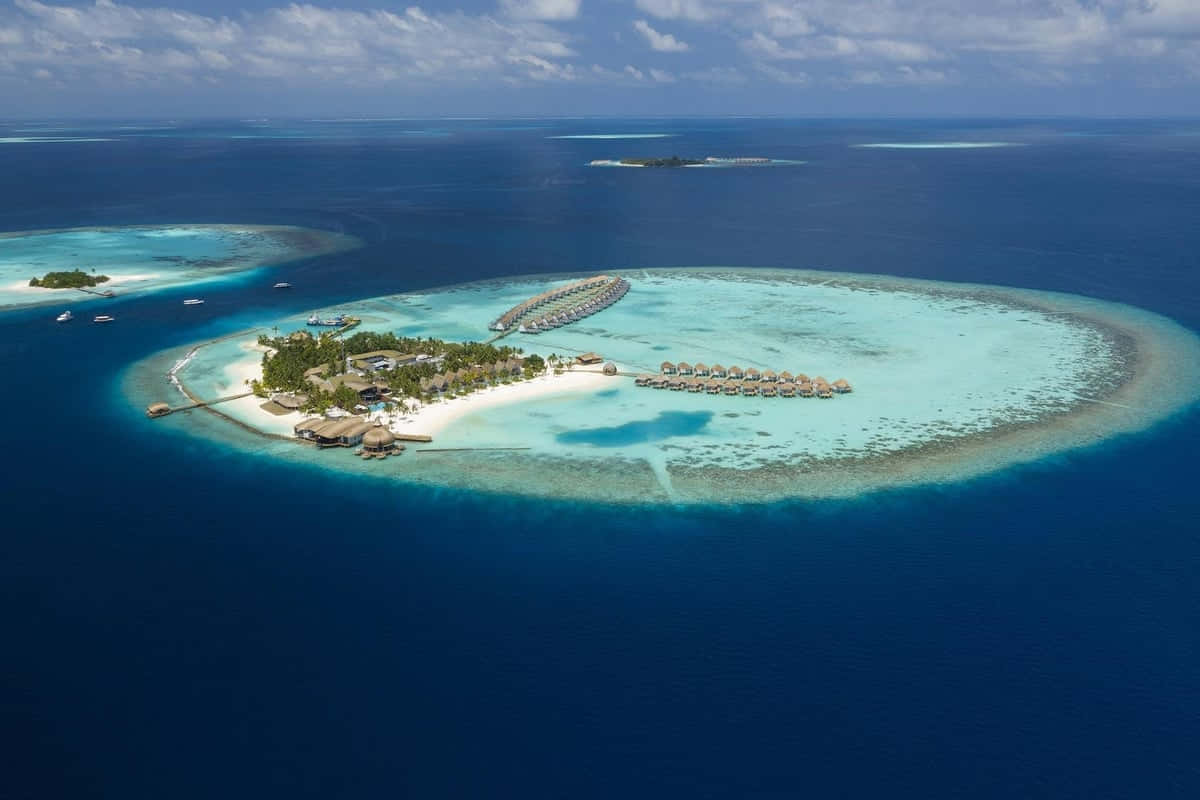 Maldives Island 桌布 壁紙 — 熱帶環礁的鳥瞰圖，擁有白色沙灘、碧綠潟湖和水上平房，四周環繞著深藍色海洋。