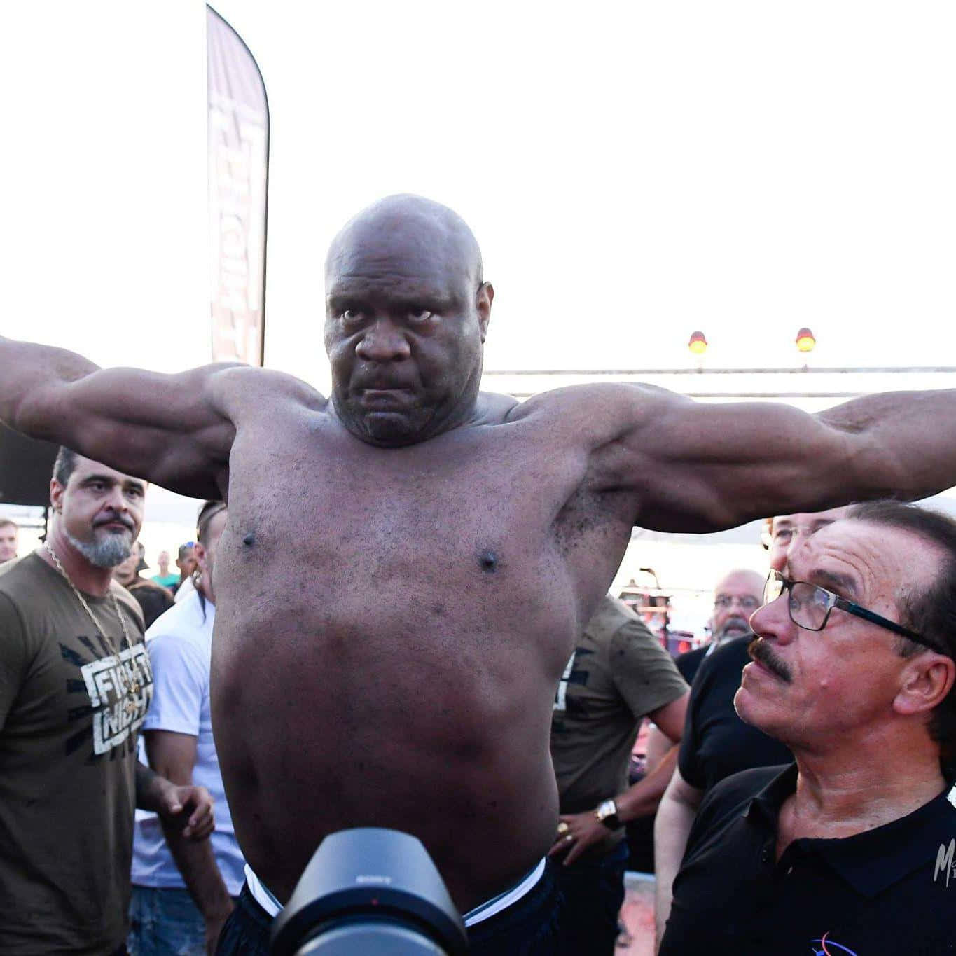 熱情與堅定的 Bob Sapp 壁紙 — 一個肌肉發達的光頭男子在戶外活動中張開雙臂，周圍有觀眾圍觀。