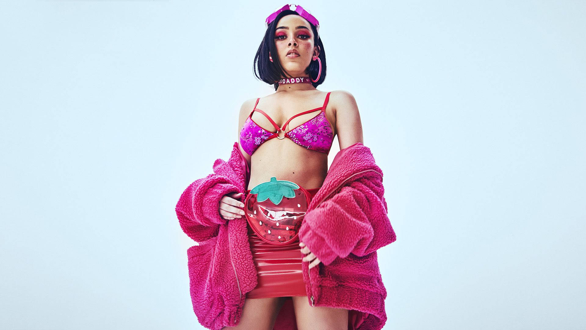 熱粉紅Doja Cat 壁紙 — 一位穿著鮮豔粉紅色內衣和毛絨外套的女性，在純淺藍色背景前自信地擺姿勢。