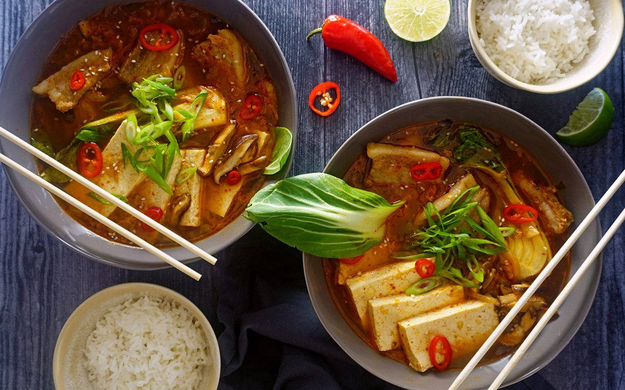 木桌上兩碗韓式辣豆腐鍋，配米飯和青檸裝飾。