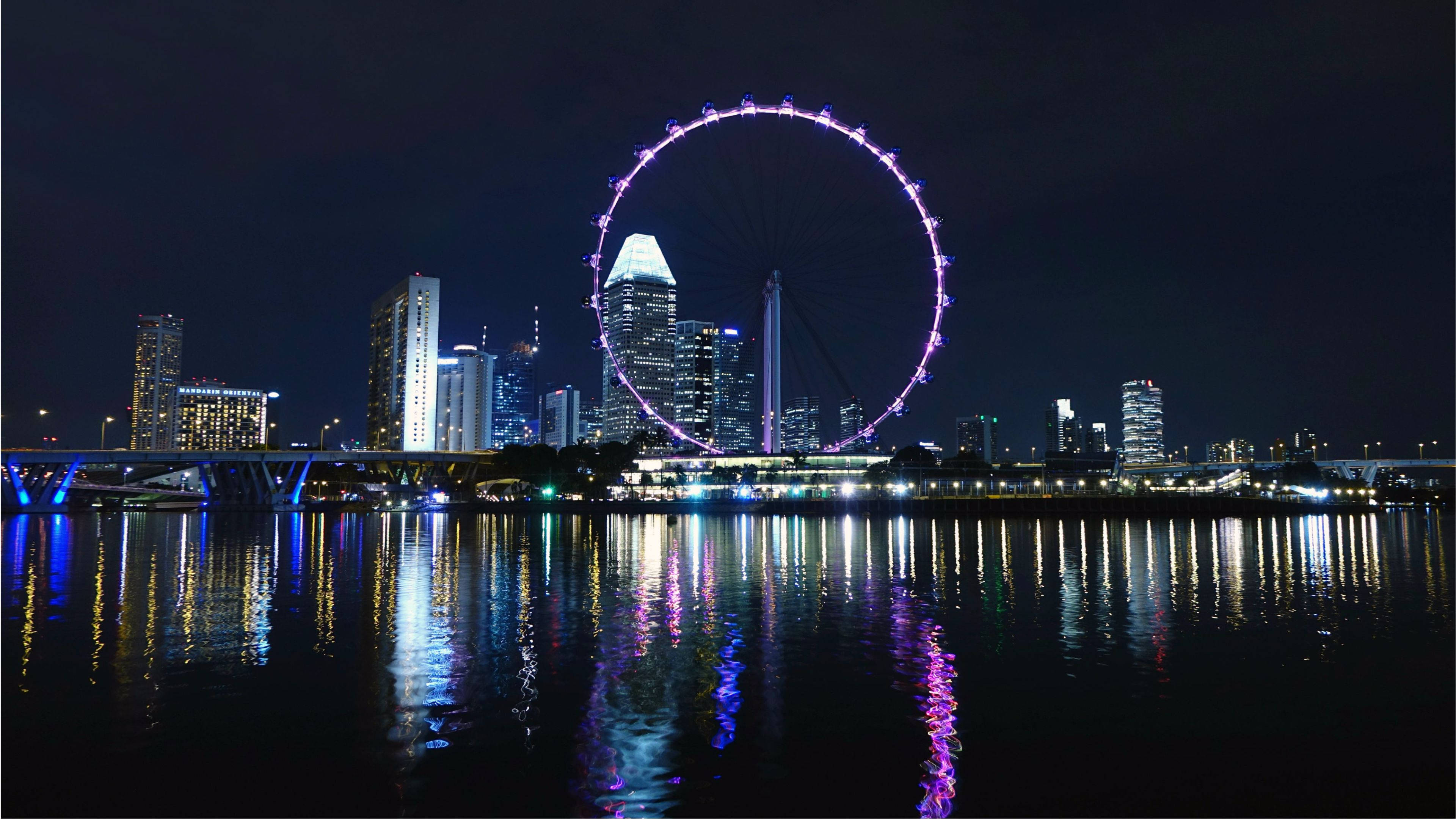 夜晚的新加坡天際線，摩天輪亮起，城市燈光倒映在水中。
