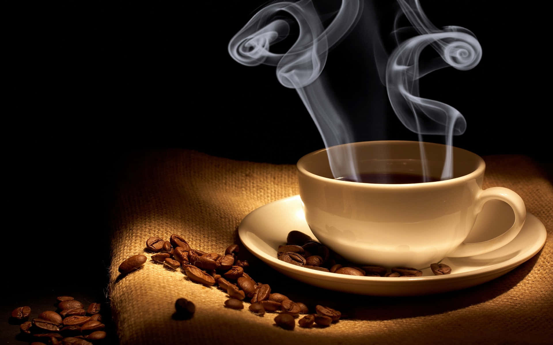 暖光下麻布上的咖啡豆和冒煙的咖啡杯。
