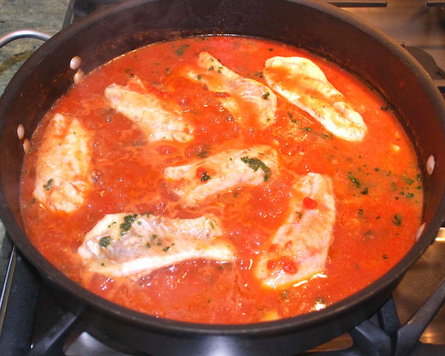 熱騰騰魚肉布魯德特燉菜 壁紙 — 新鮮魚柳在爐灶上的深色煎鍋中，用充滿活力的番茄醬和香草慢燉。