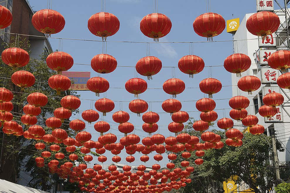熱鬧的春節慶祝 壁紙 — 鮮豔的紅色燈籠密密麻麻地掛在繁華街道上方，襯著晴朗的藍天。