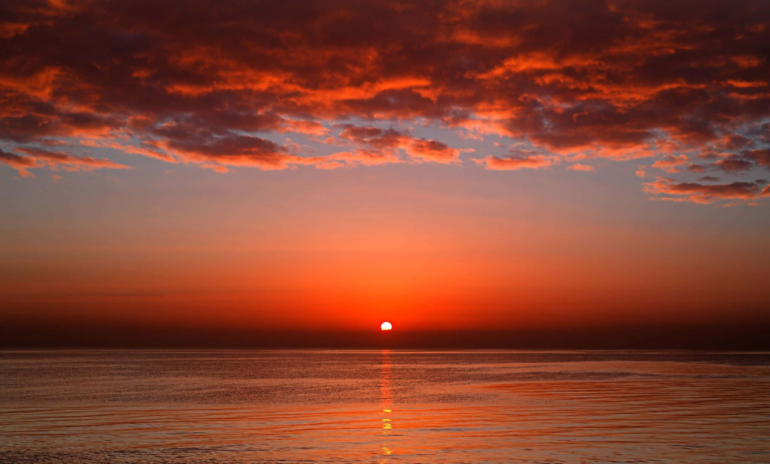 Red Sunset 桌布 壁紙 — 熾熱的夕陽將天空和寧靜的海洋塗上鮮豔的橙色和紅色色調，太陽沉入地平線以下。