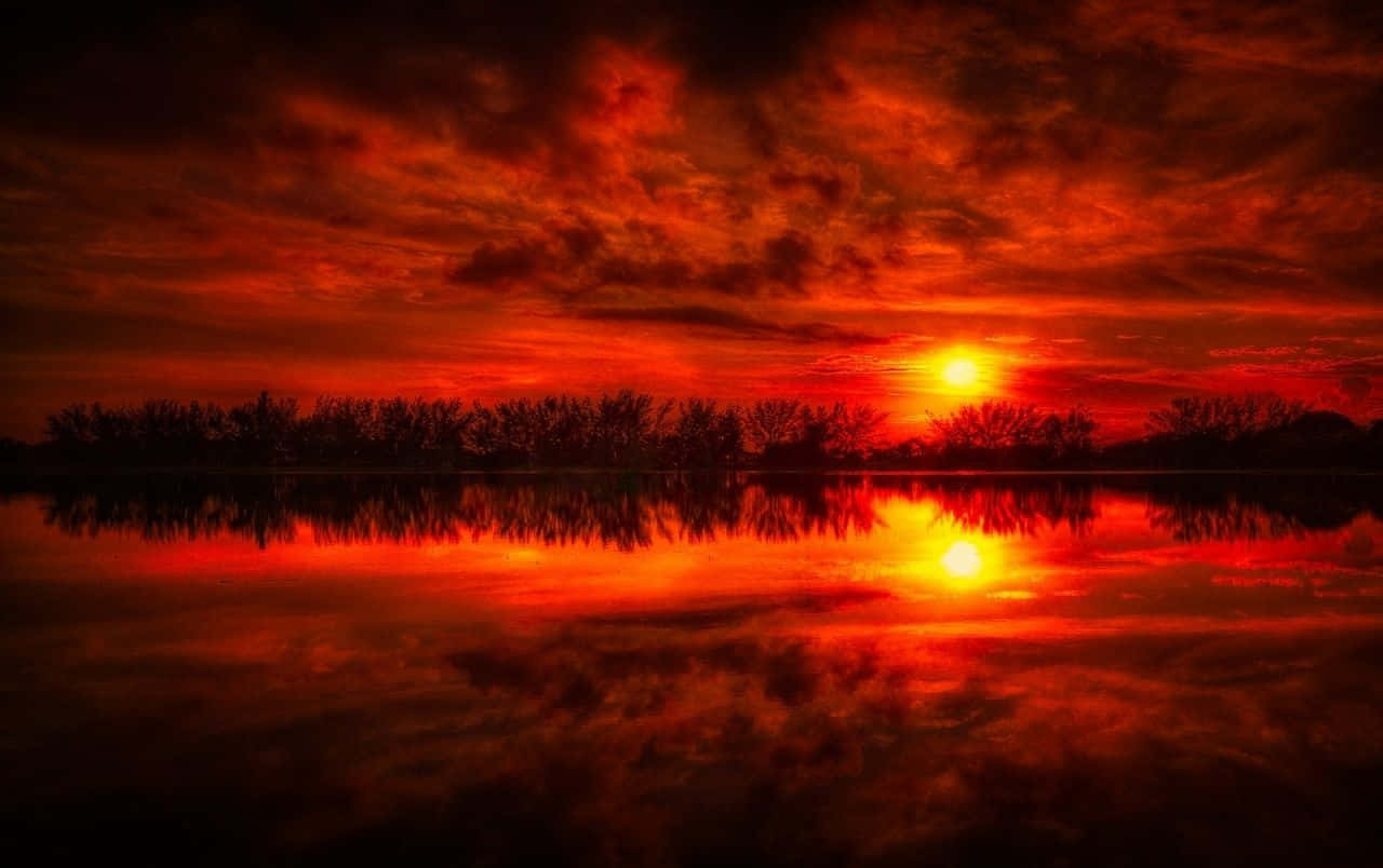 Red Sunset 桌布 壁紙 — 熾熱的夕陽將天空和水面染成鮮豔的紅色和橙色，雲彩完美地倒映在平靜的水面上。